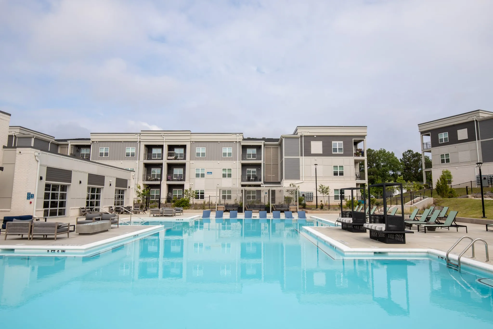 Multifamily community resort pool with loungers along the water and the apartment buildings behind