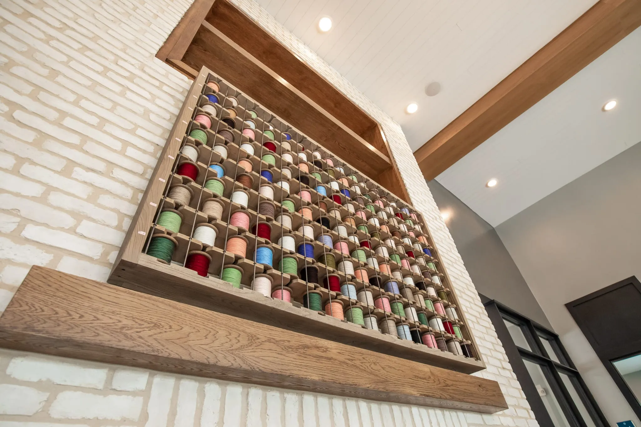 Multifamily amenity interior detail: thread spool display, coloured spools set in a wood case mounted on white brick