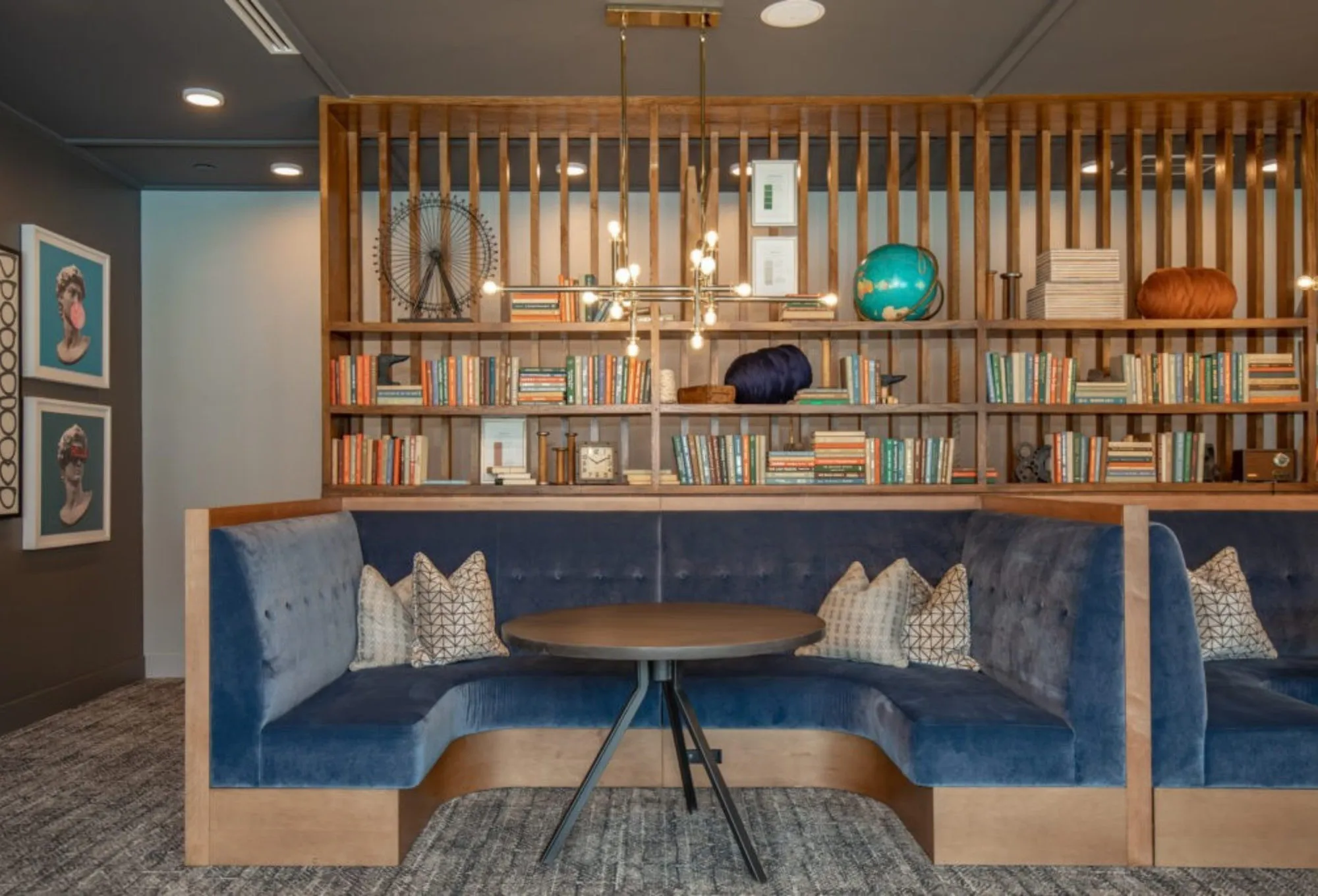 Blue velvet U-shaped banquette under a slatted bookcase wall of colour-sorted books, lit by a brass sputnik chandelier