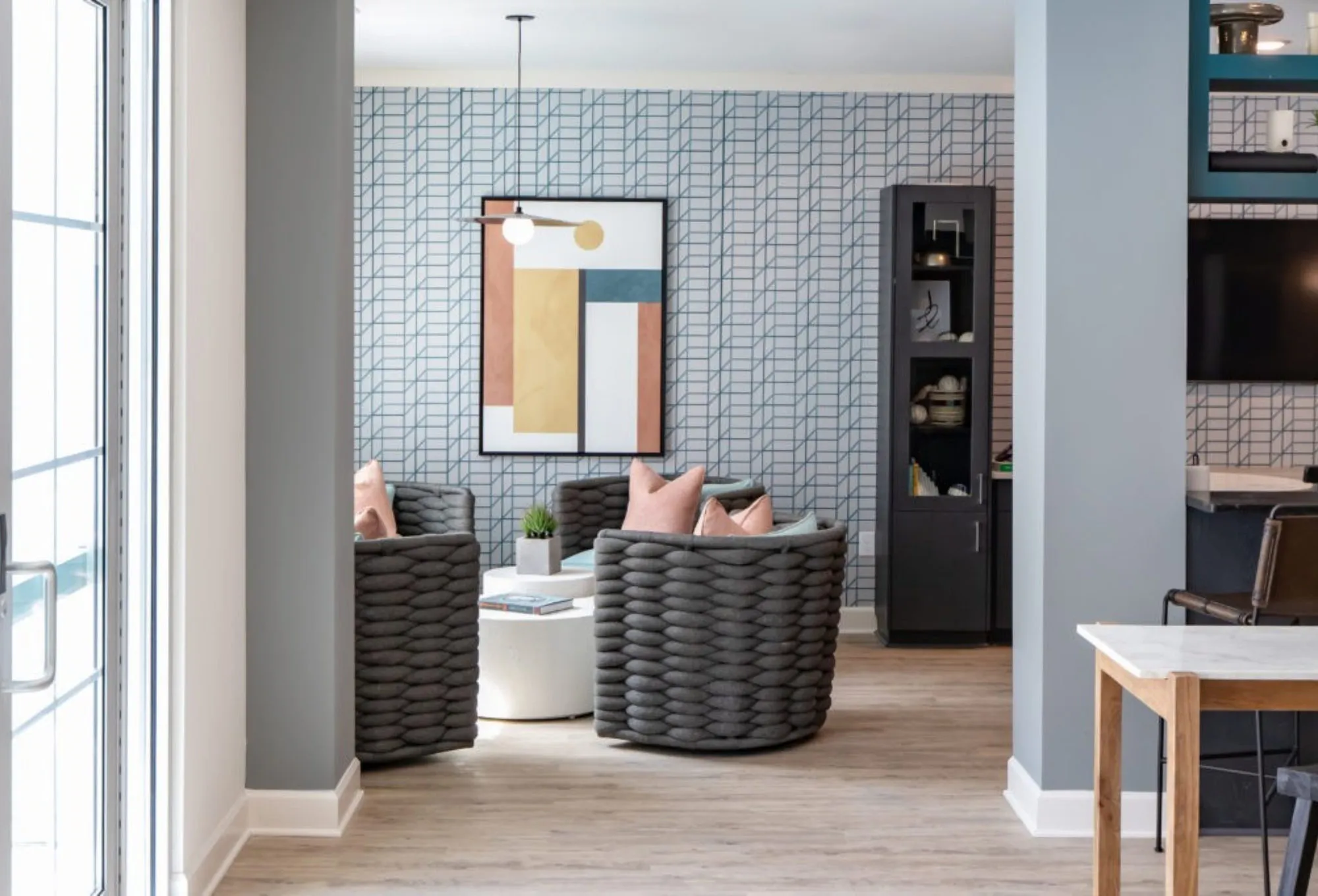 Co-working nook with blue geometric wallpaper, two woven barrel chairs at a white round table and a colour-block print
