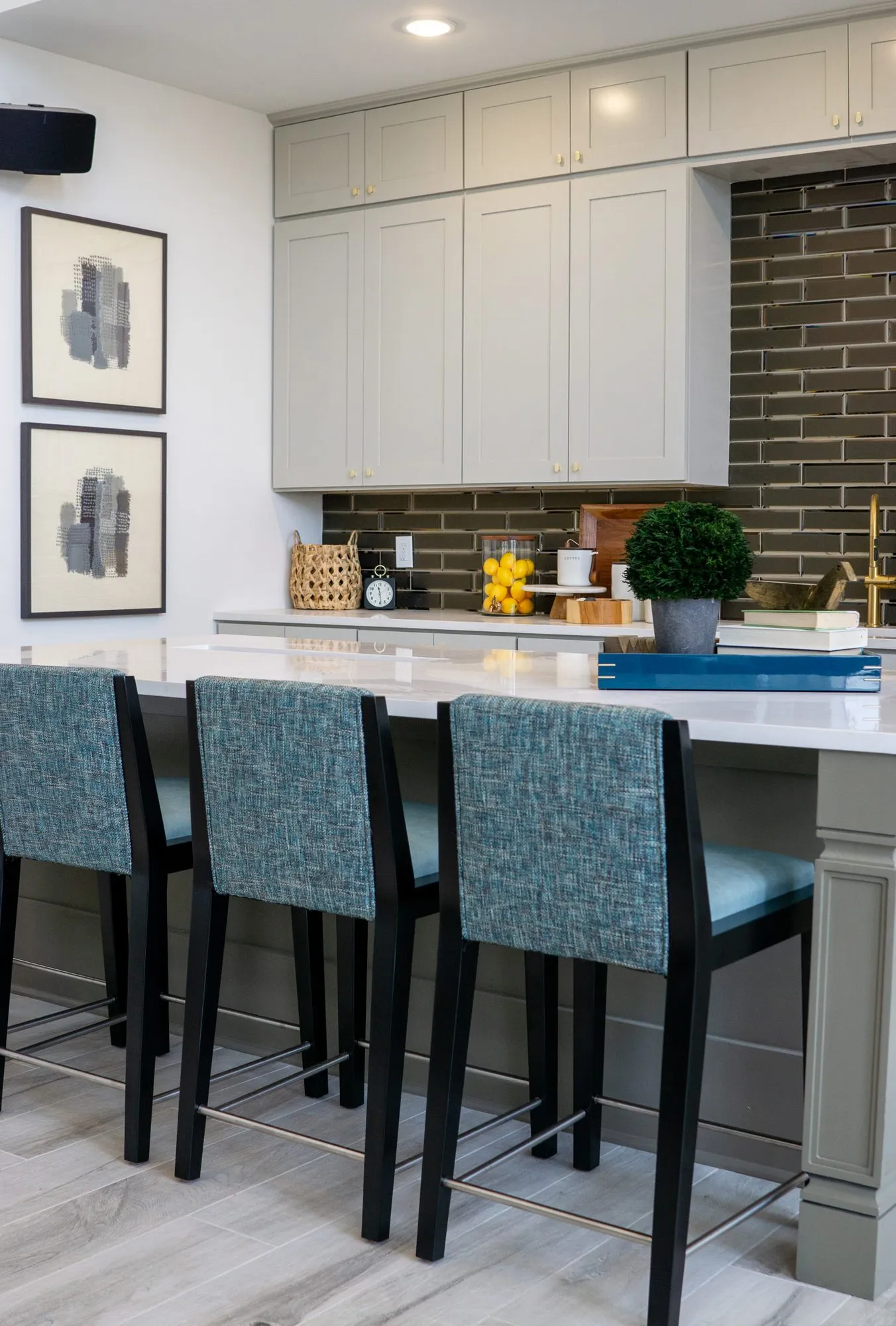 Multifamily kitchen island with teal upholstered stools, pale grey cabinetry and a charcoal brick tile backsplash