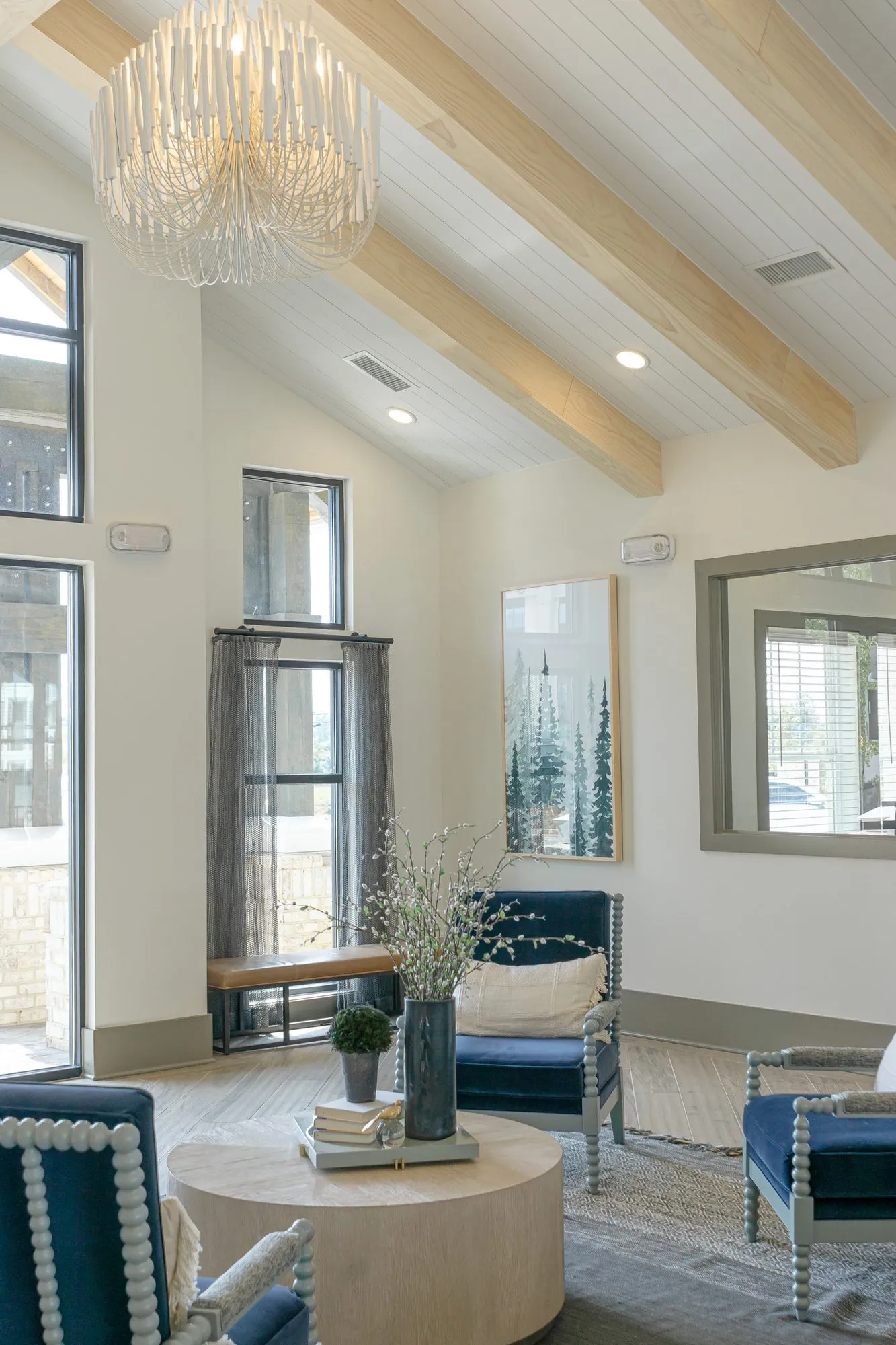 Multifamily amenity lounge with navy spindle chairs and a round wood table under a beaded chandelier and pale timber beams