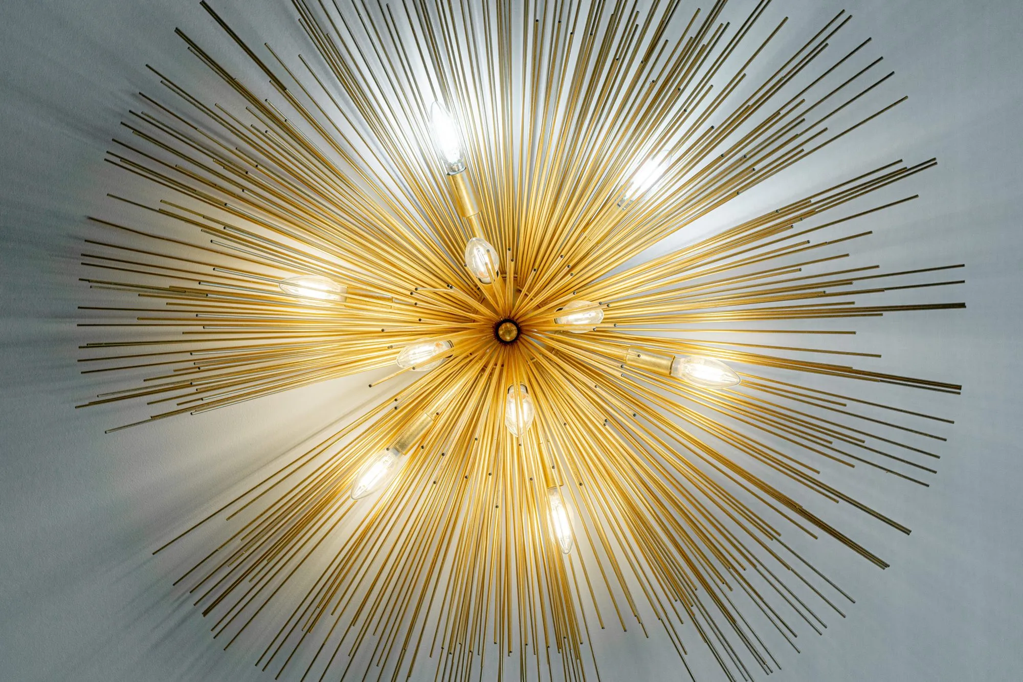 Multifamily interior detail: looking up at a gold starburst ceiling light with exposed bulbs