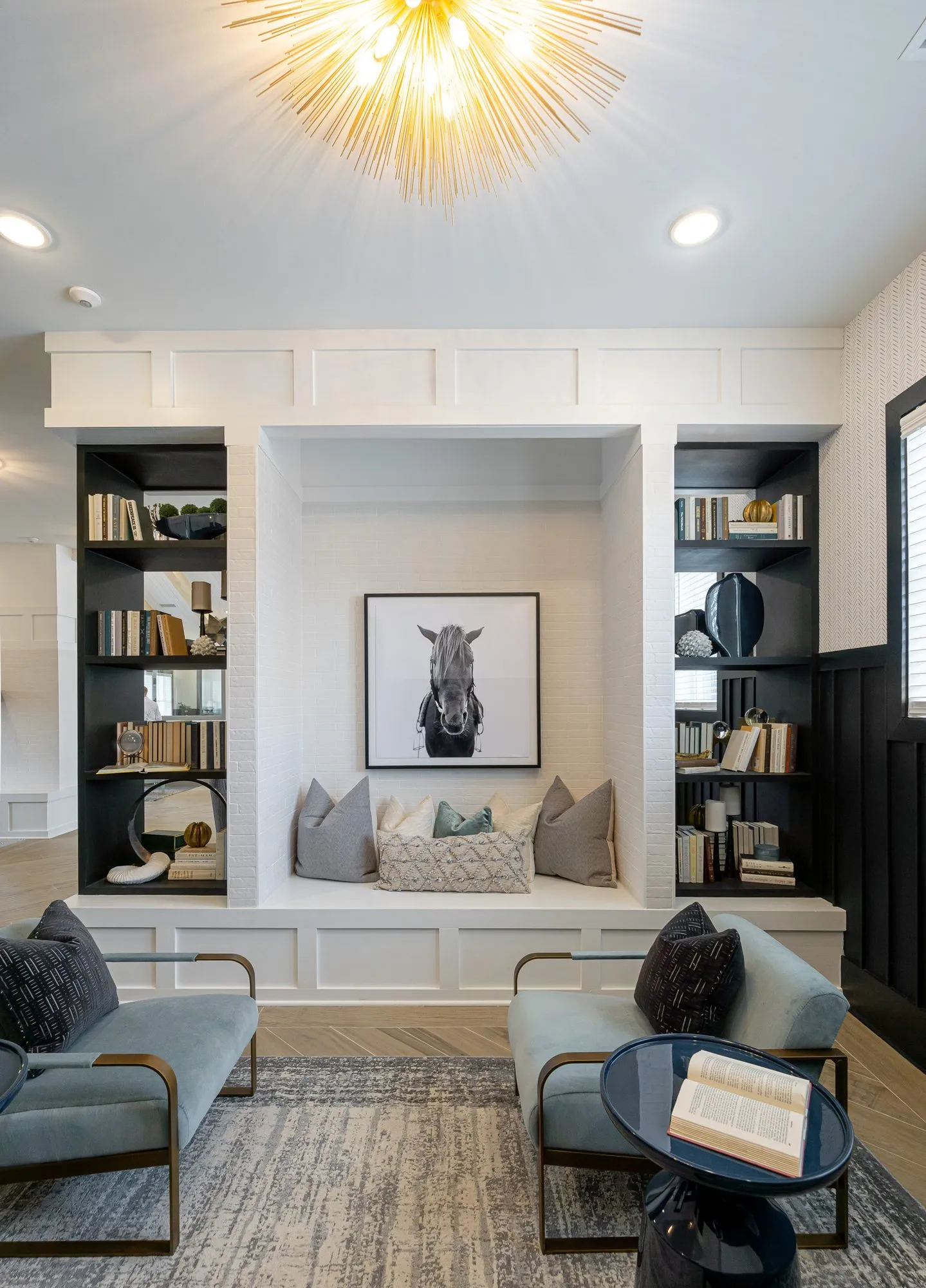 Multifamily amenity library with a cushioned bench alcove under a gold starburst light, a horse portrait between bookshelves