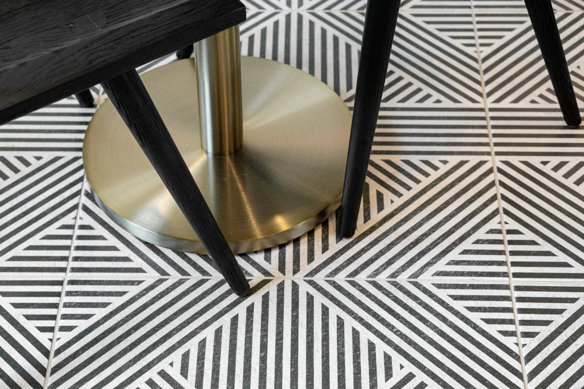 Multifamily interior detail: brass table base and black chair legs on black and white geometric floor tile