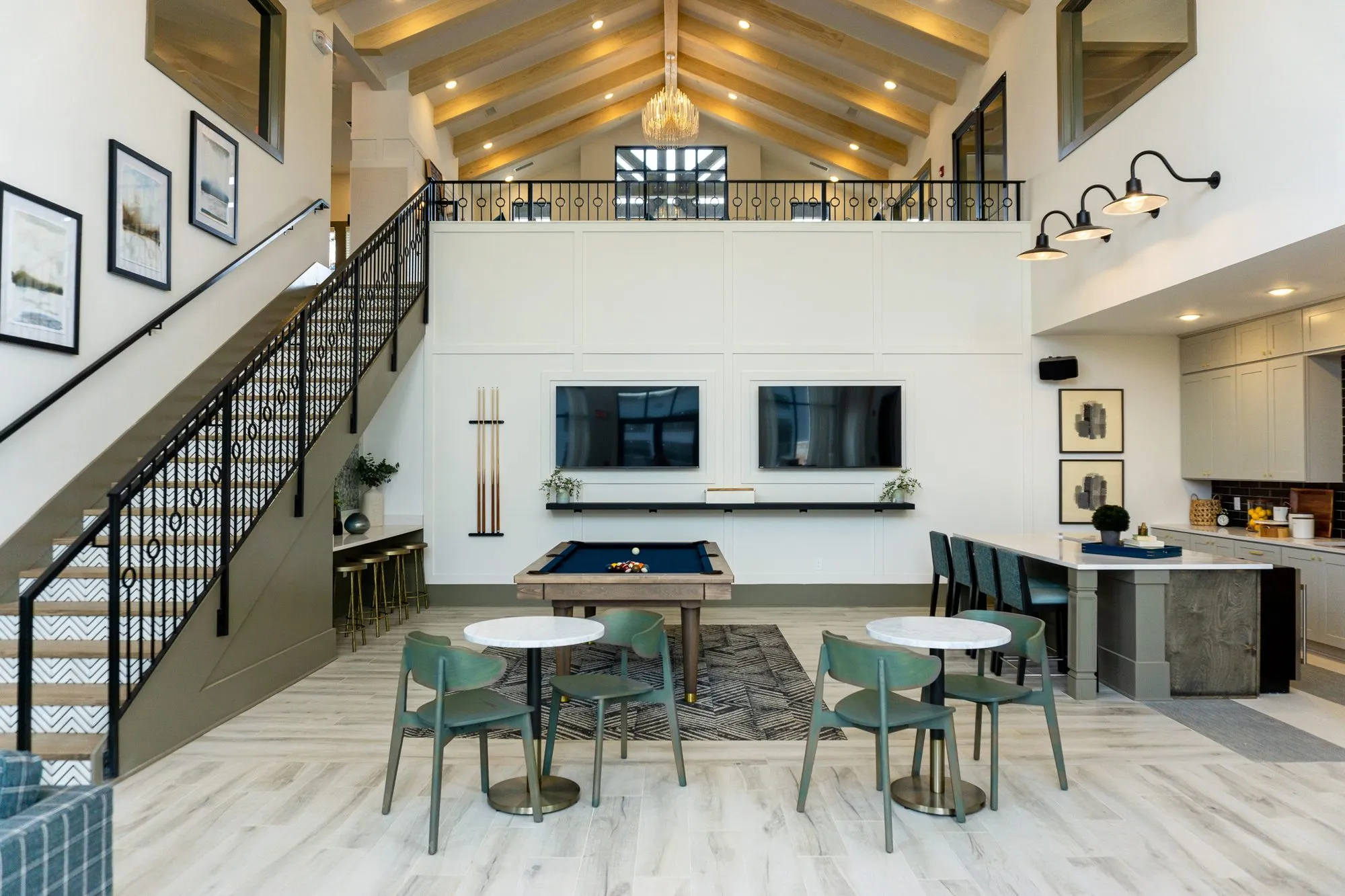 Multifamily amenity double-height clubroom under a timber vault, billiards and cafe tables below the iron mezzanine rail