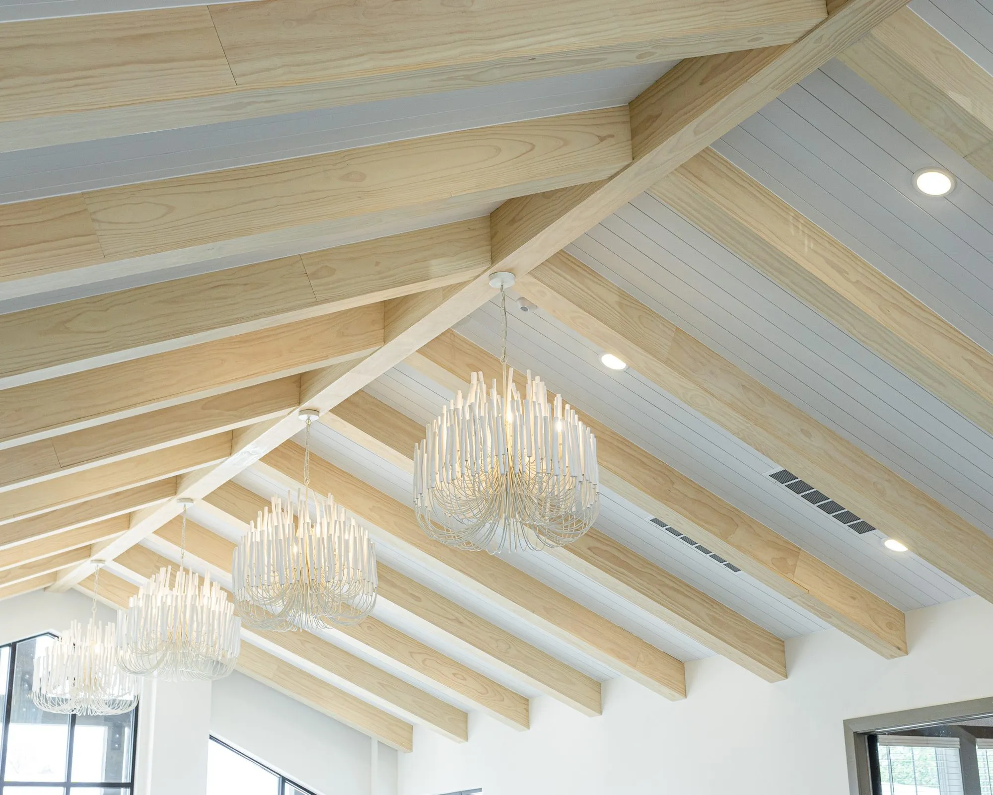 Multifamily interior detail: pale timber beams on a white tongue and groove vault hung with tiered crystal chandeliers