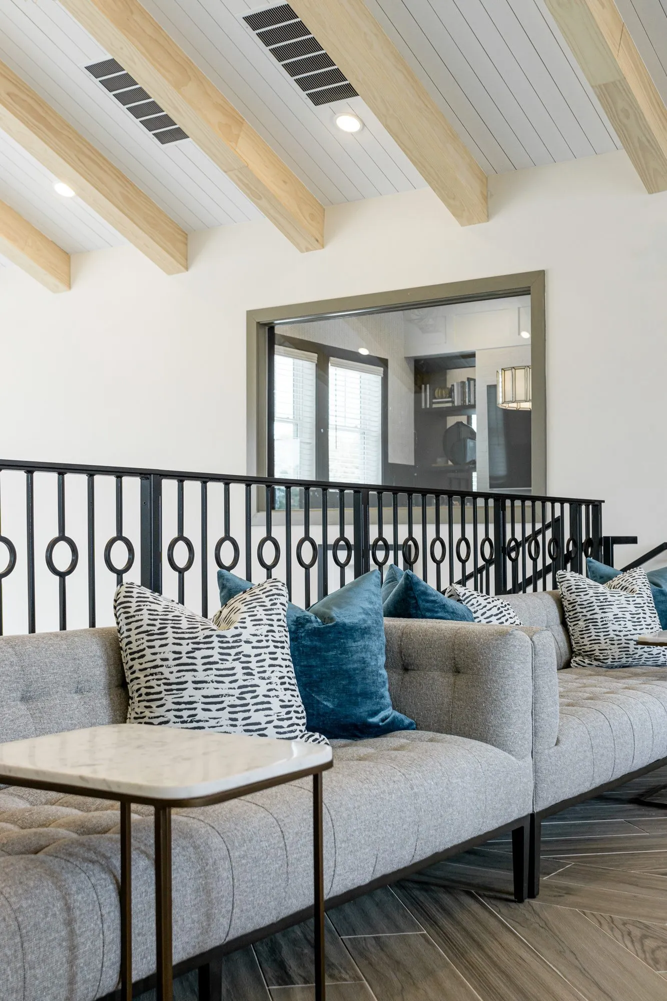 Multifamily interior detail: grey tufted sofa with blue and patterned pillows and a marble side table, iron rail behind