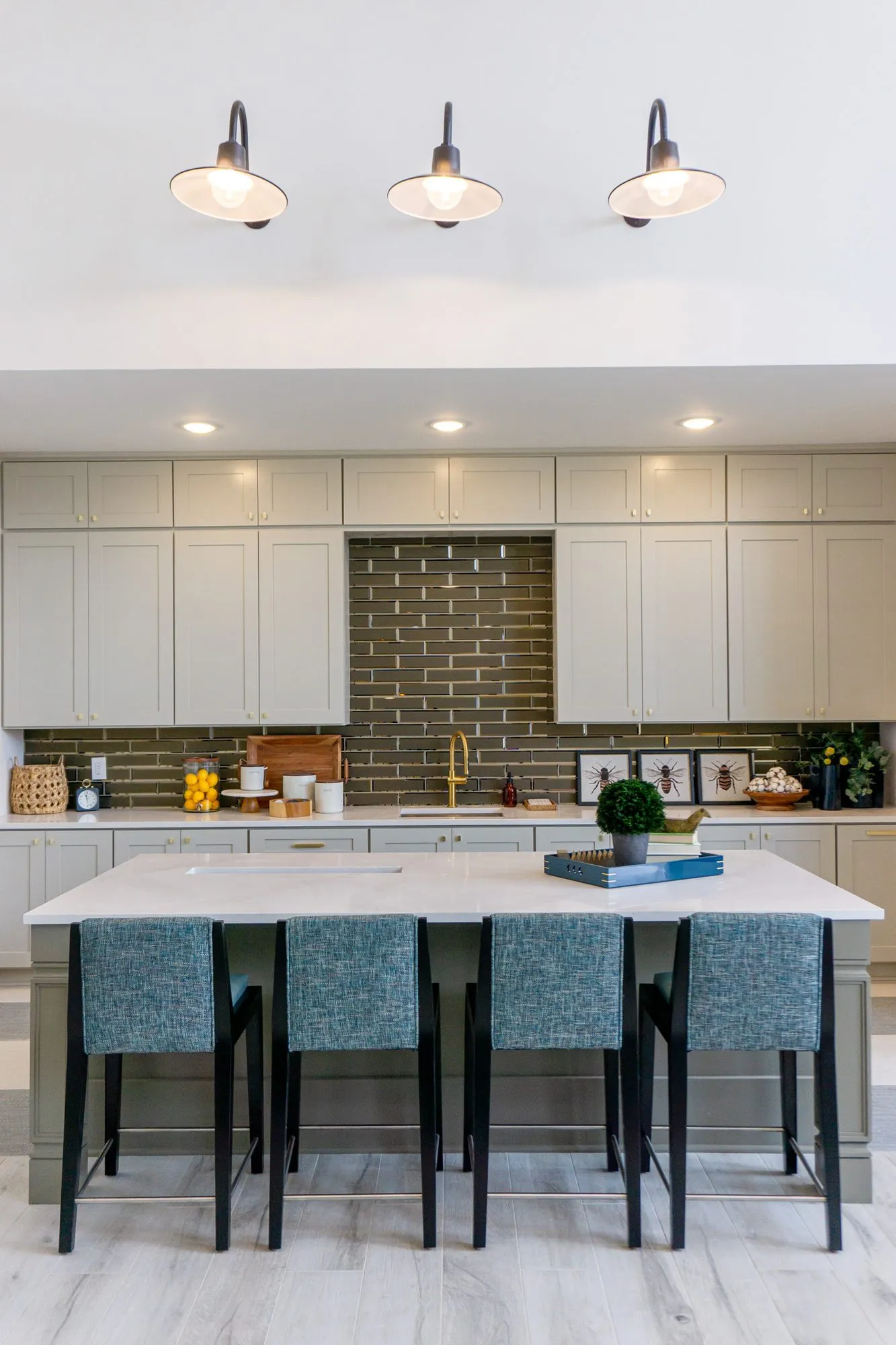 Multifamily kitchen island with four teal stools below three black barn sconces and grey cabinetry