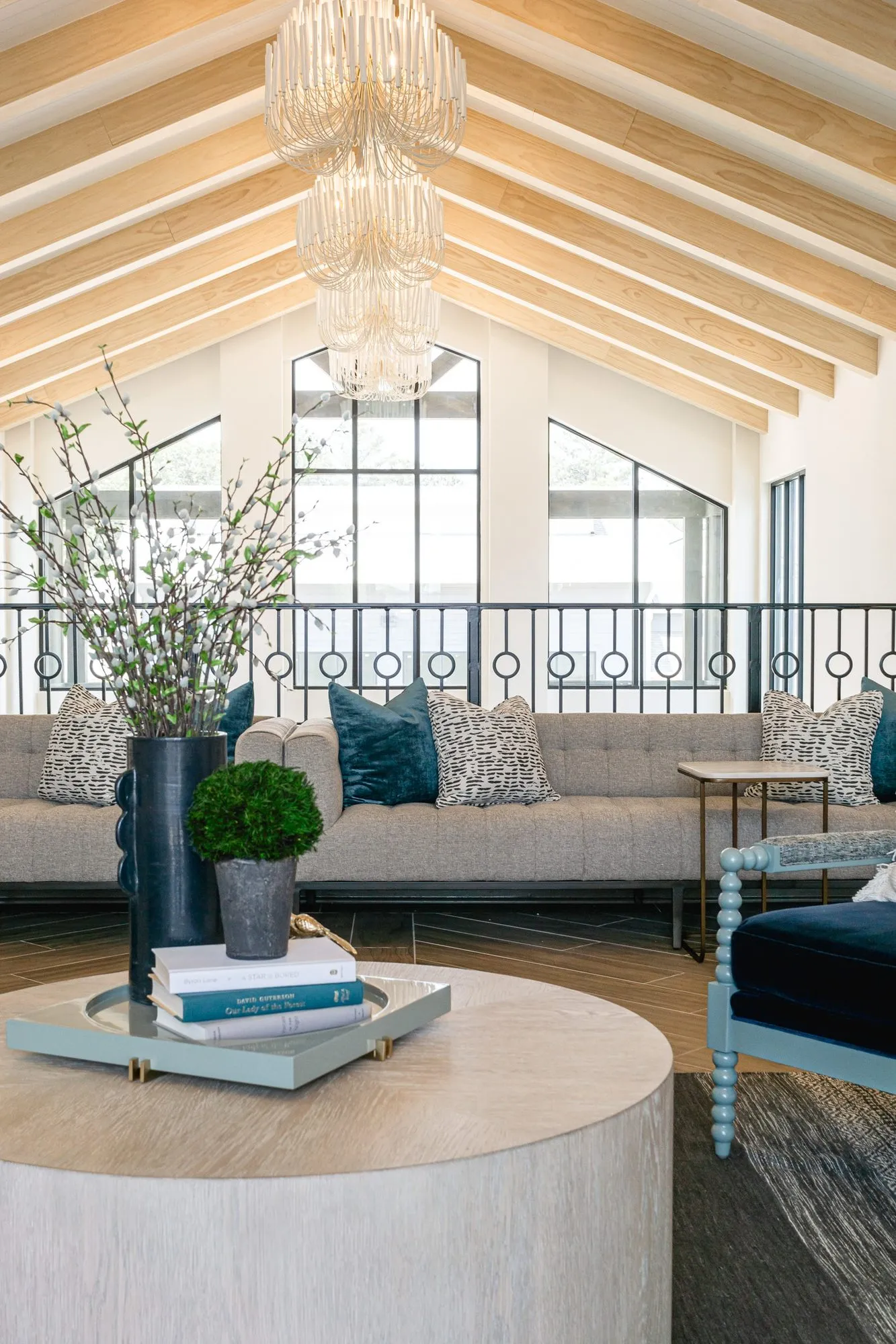 Multifamily amenity mezzanine lounge with a grey tufted sofa along the iron rail under a tiered glass chandelier