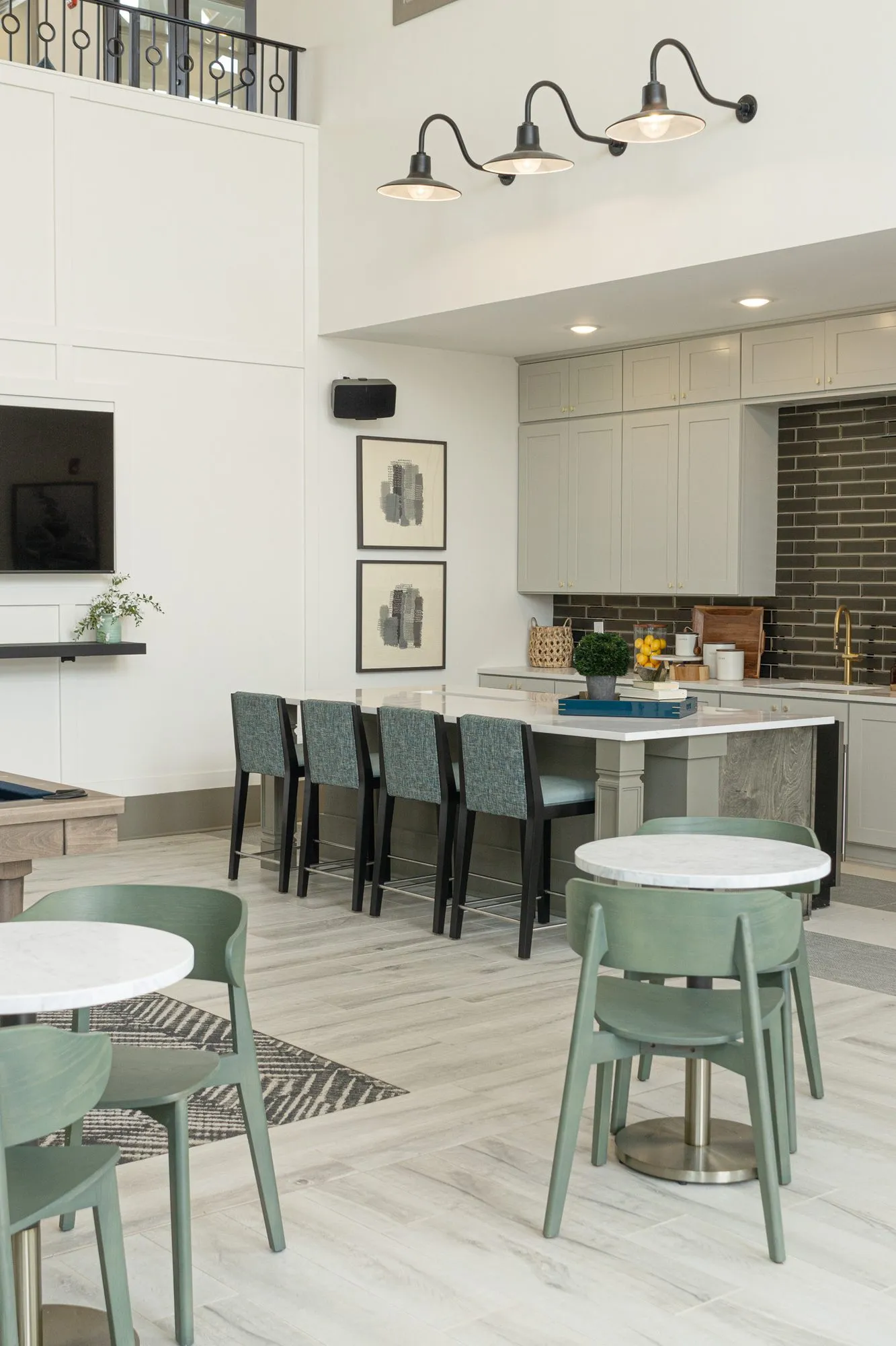 Multifamily kitchen island with teal stools under barn sconces, sage cafe chairs at marble tables in front