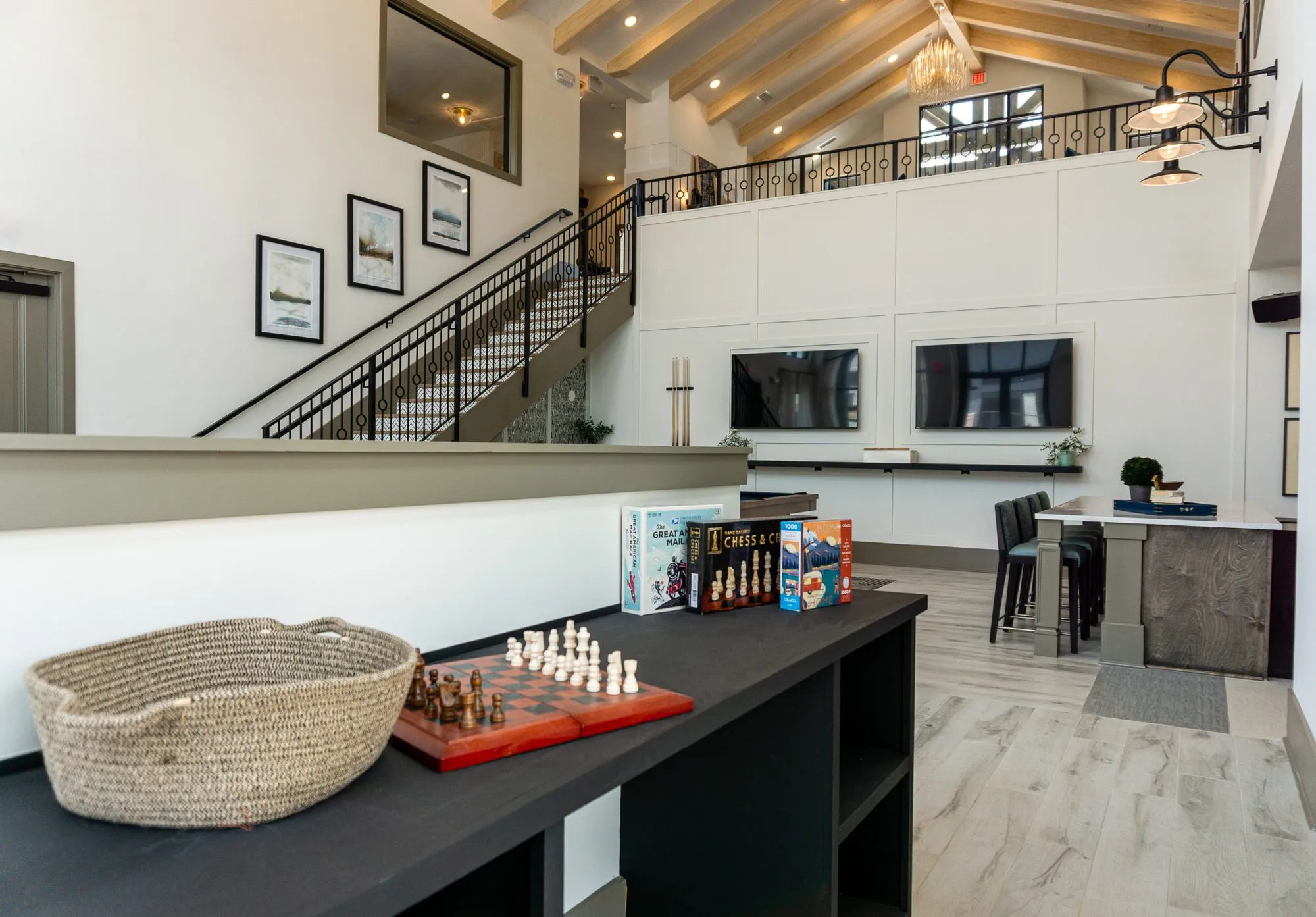 Multifamily amenity clubroom: chess set and board games on a dark ledge overlooking the double-height room, stair and kitchen