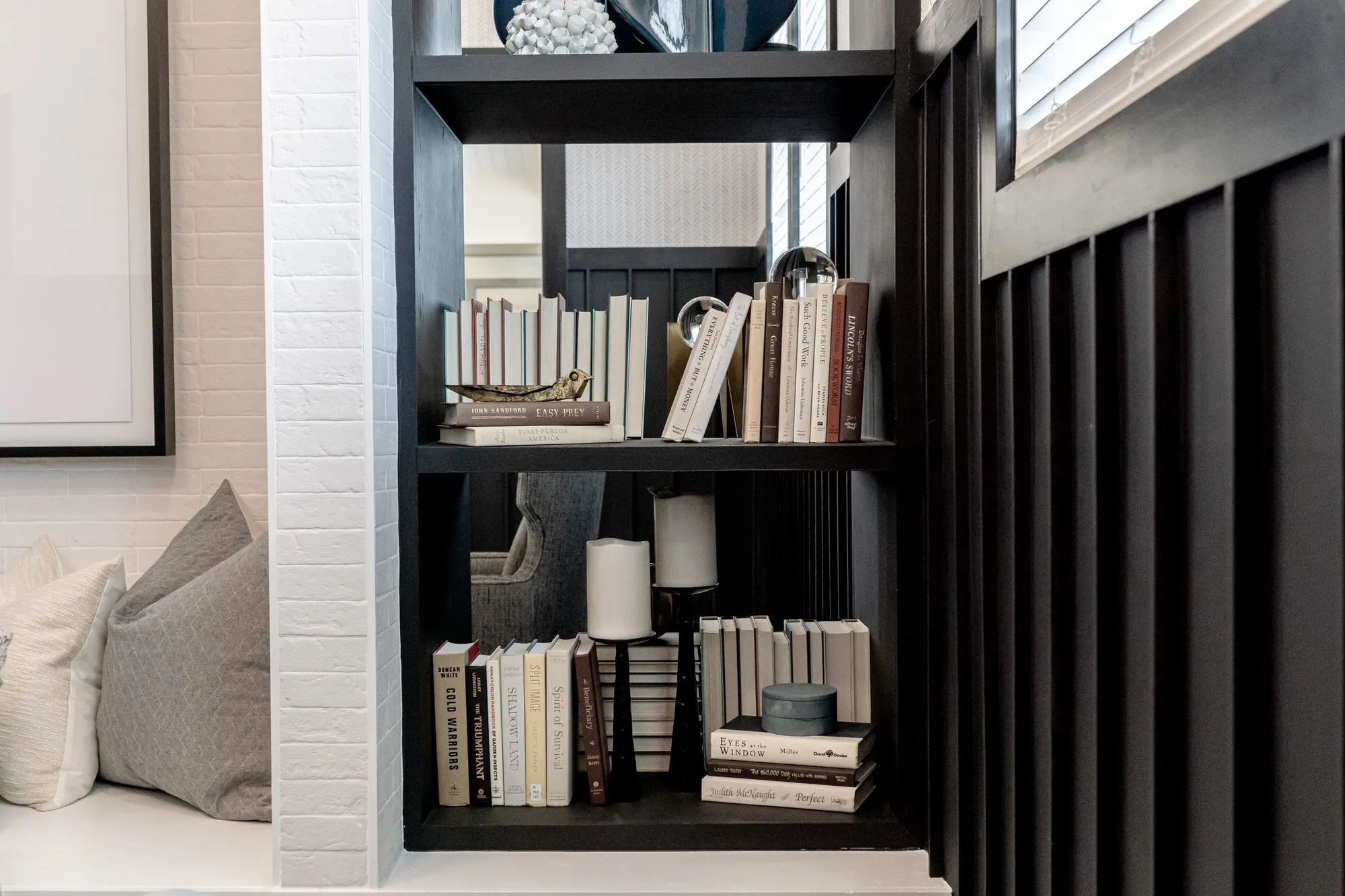 Multifamily interior detail: black bookshelf with books and candles beside the window seat, black board and batten wall