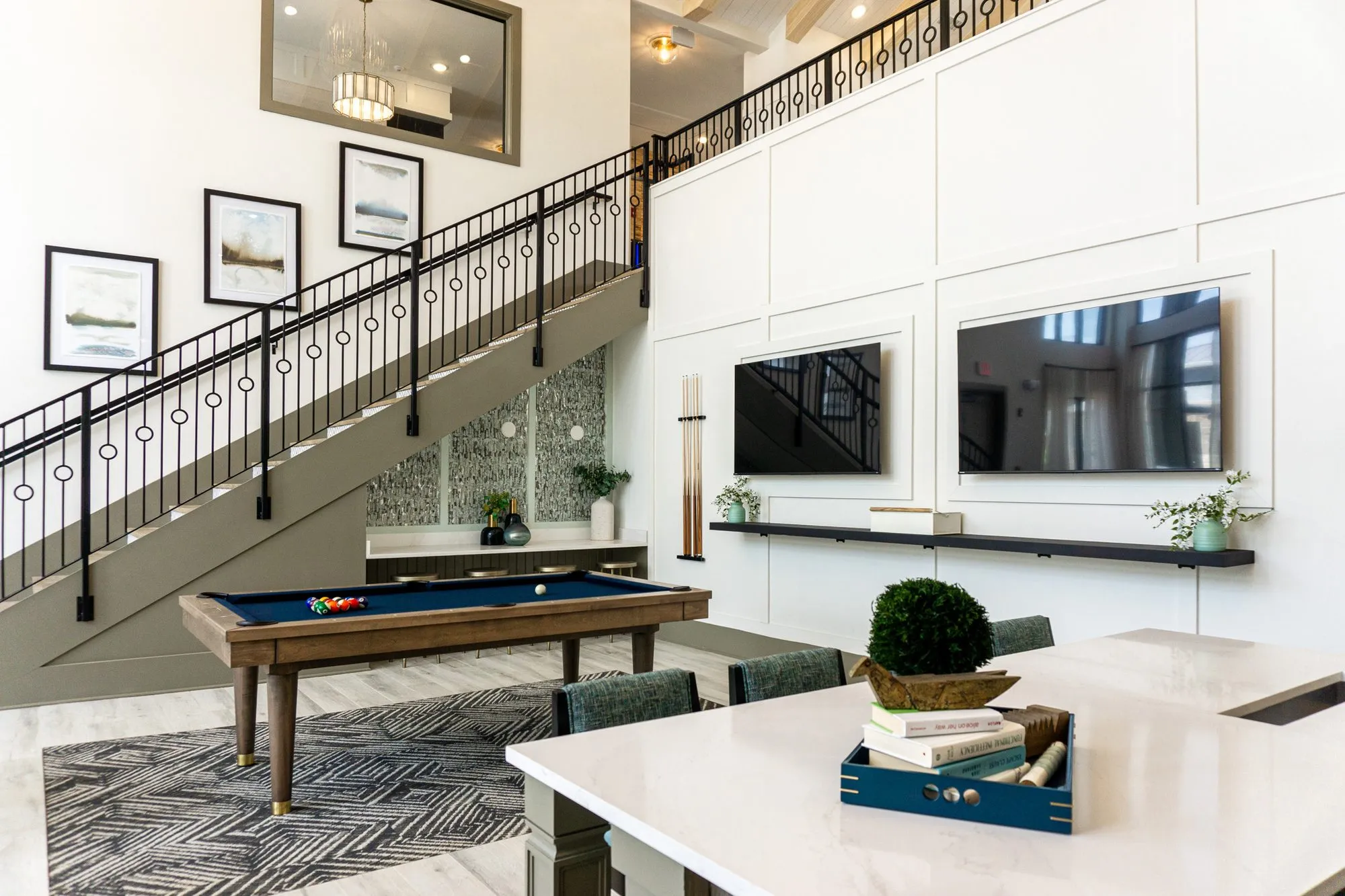 Multifamily amenity billiards table under the iron stair beside the white panelled screen wall, seen from the kitchen island