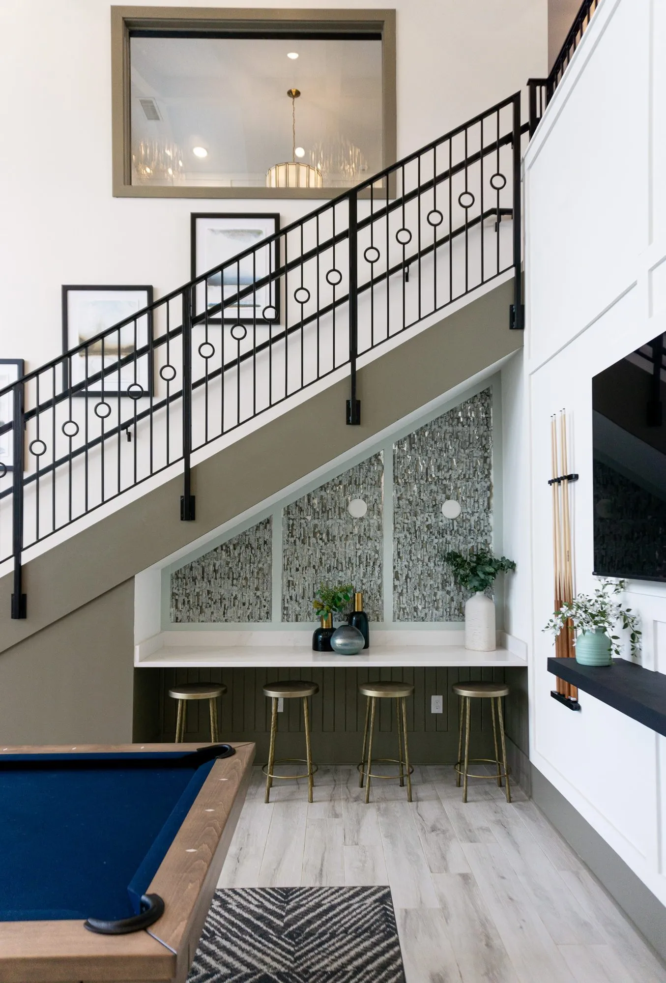 Multifamily amenity clubroom with an iron stair of circle balusters rising above a counter with brass stools