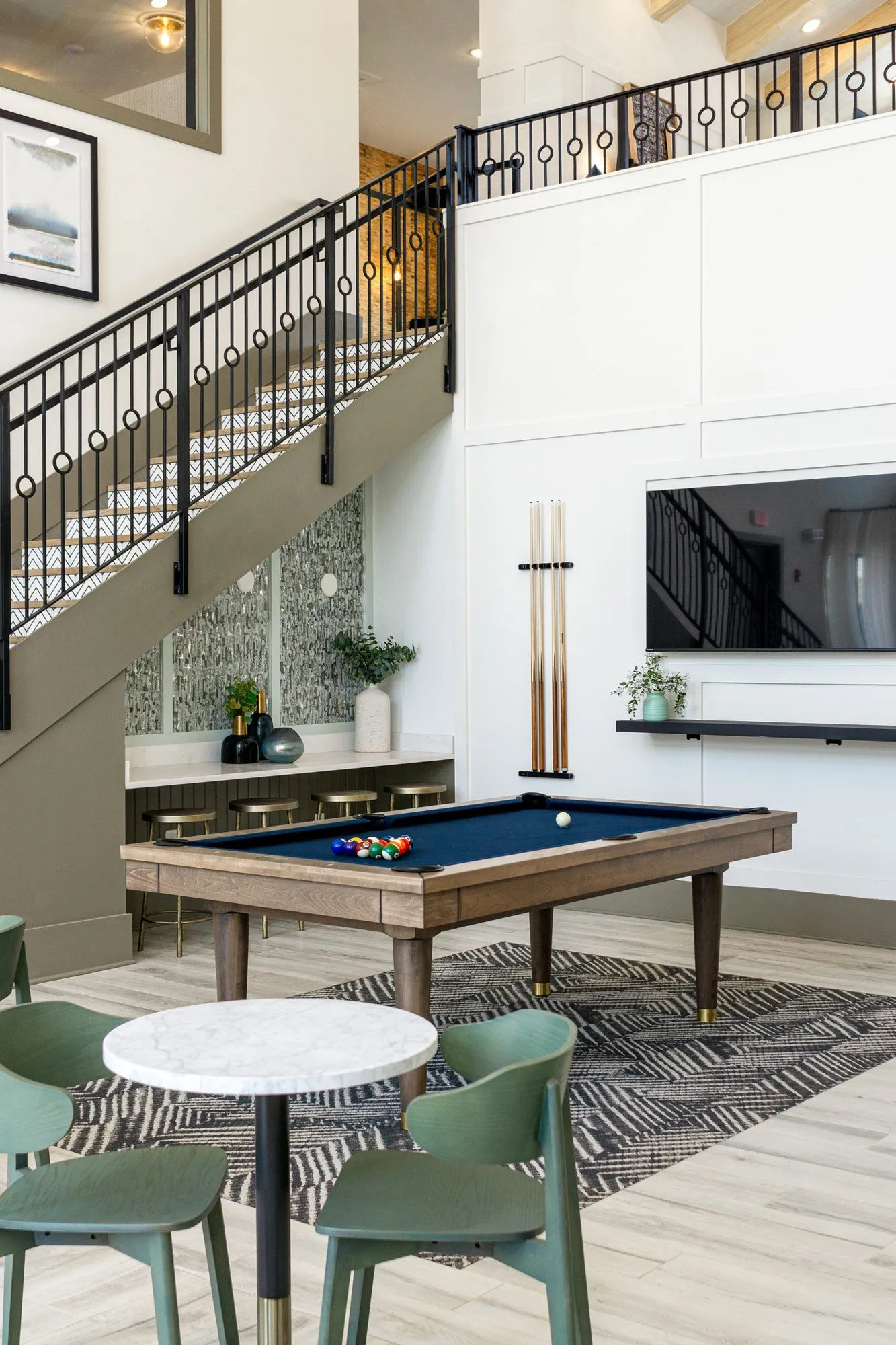 Multifamily amenity clubroom with sage cafe chairs at a marble table before the billiards table and stair alcove counter