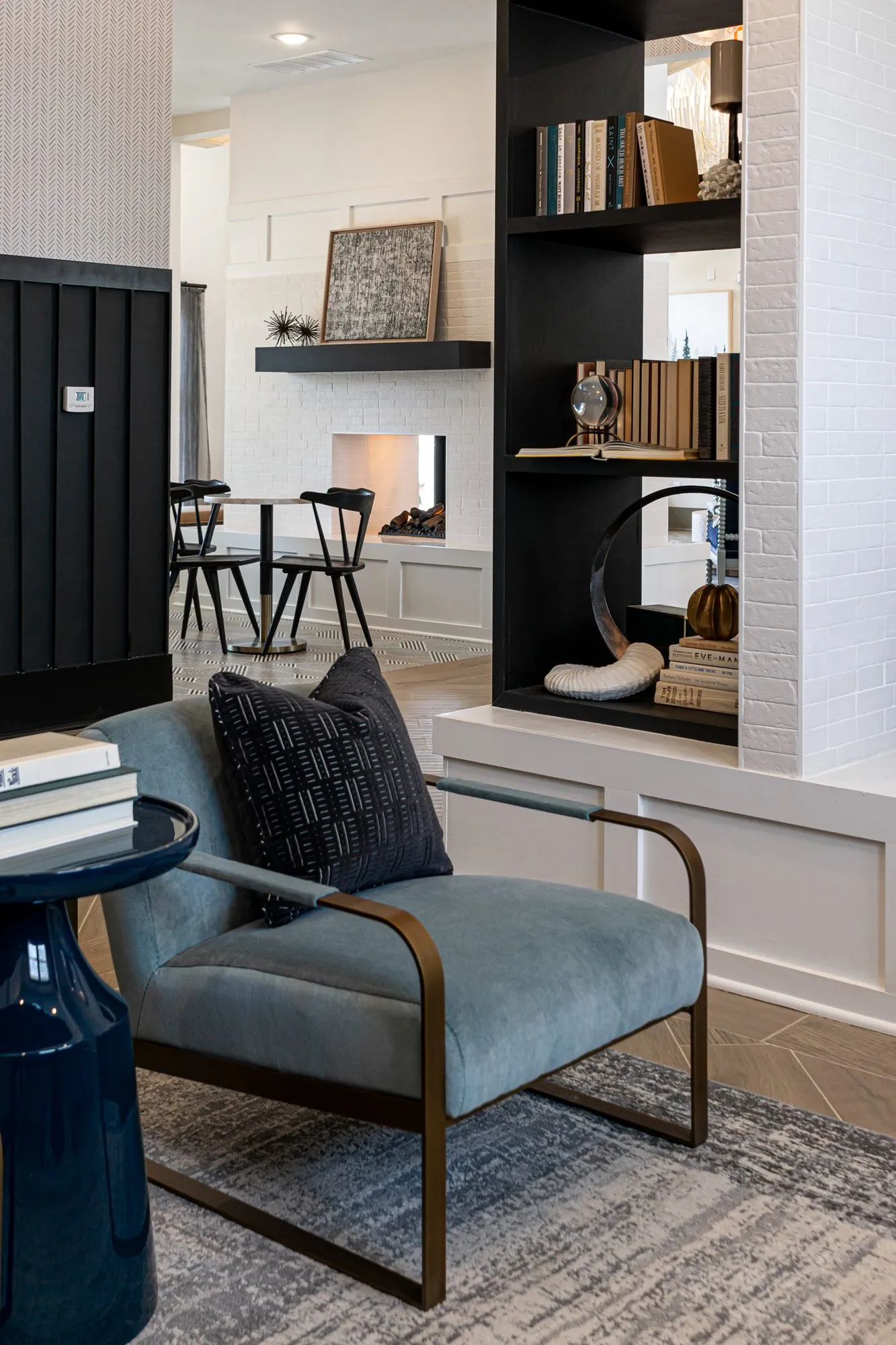 Multifamily interior detail: blue velvet armchair with a brass frame beside black shelving and a white brick divider