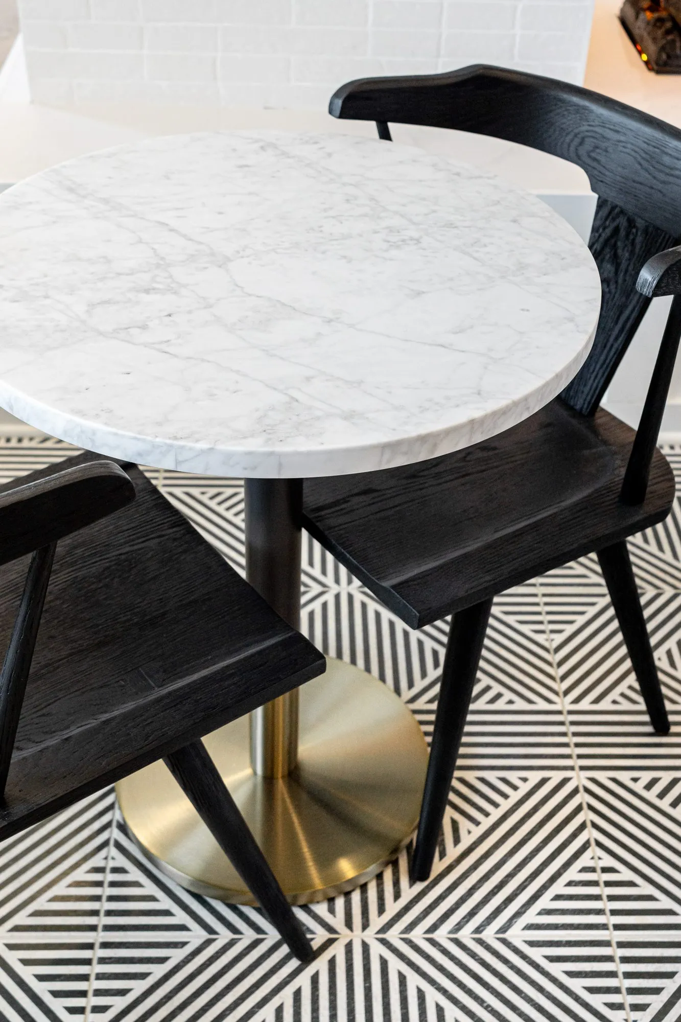Multifamily interior detail: marble cafe table on a brass base with black spindle back chairs on black and white tile