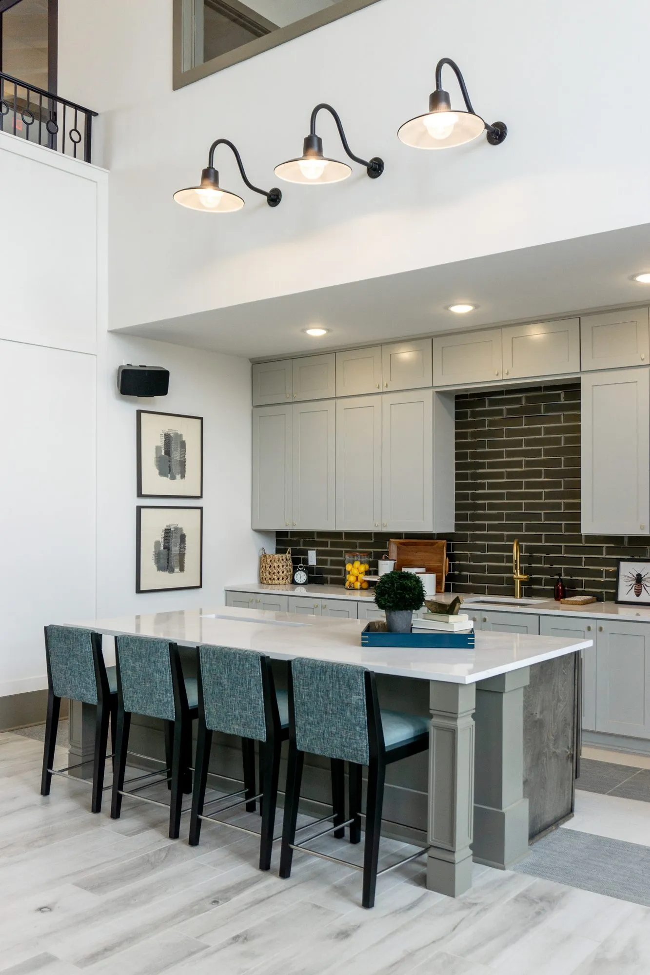 Multifamily kitchen island with teal stools below barn sconces and the mezzanine rail, seen at an angle