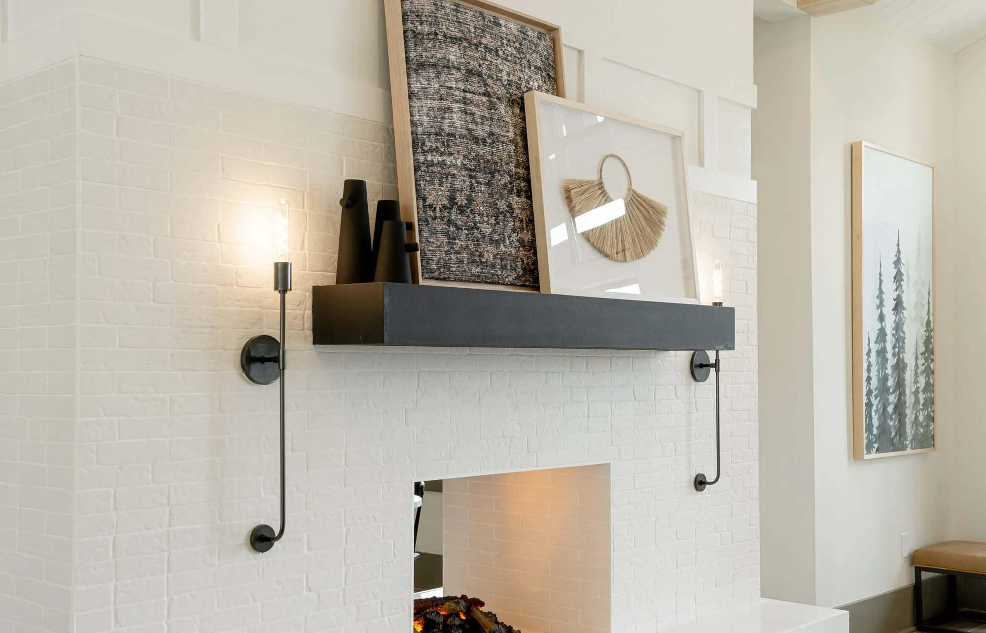 Multifamily interior detail: white brick chimney breast with a black mantel shelf, framed textile art and candle sconces