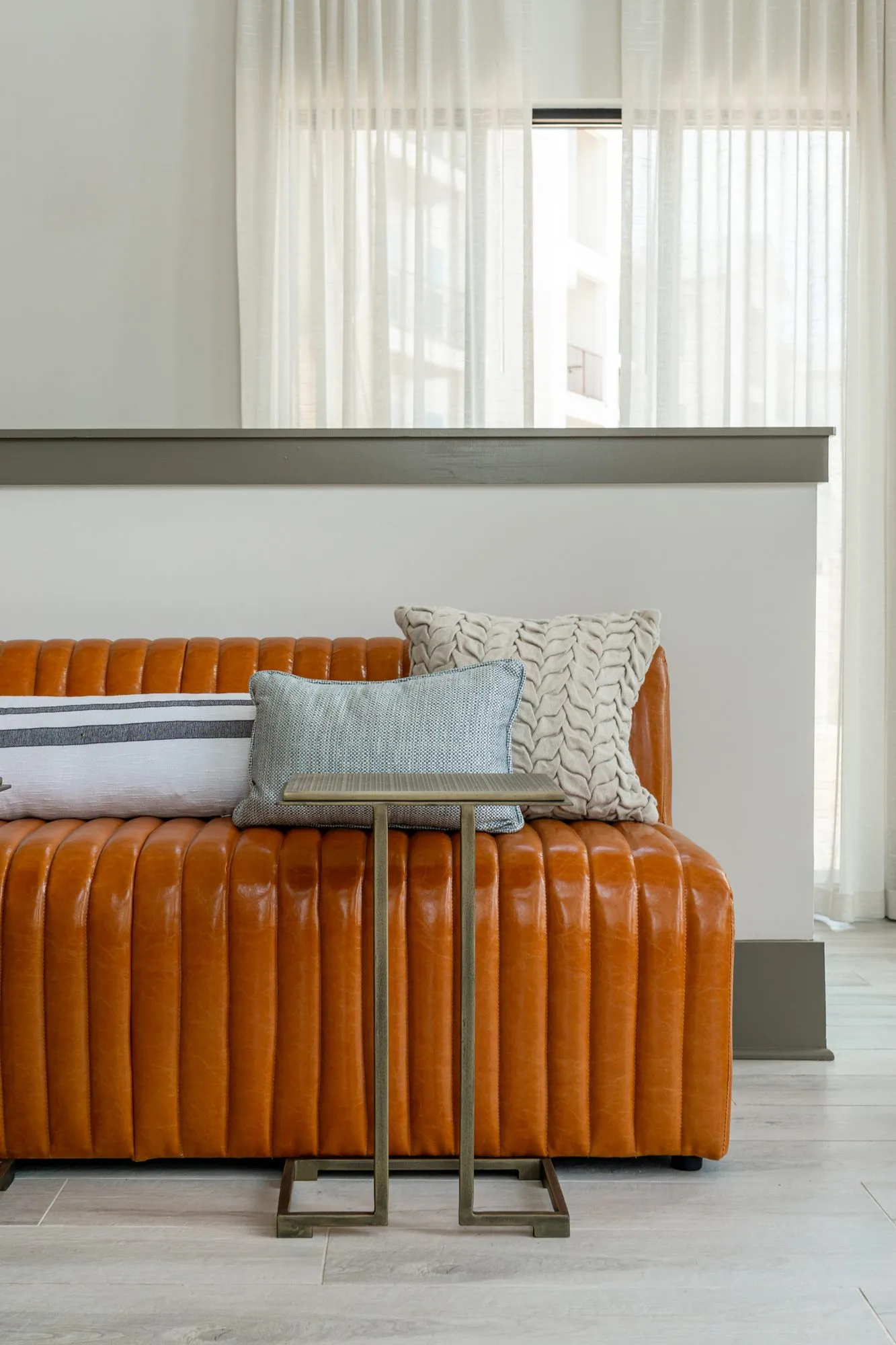 Multifamily interior detail: cognac channel tufted leather bench with pillows and a brass C-table below sheer curtains