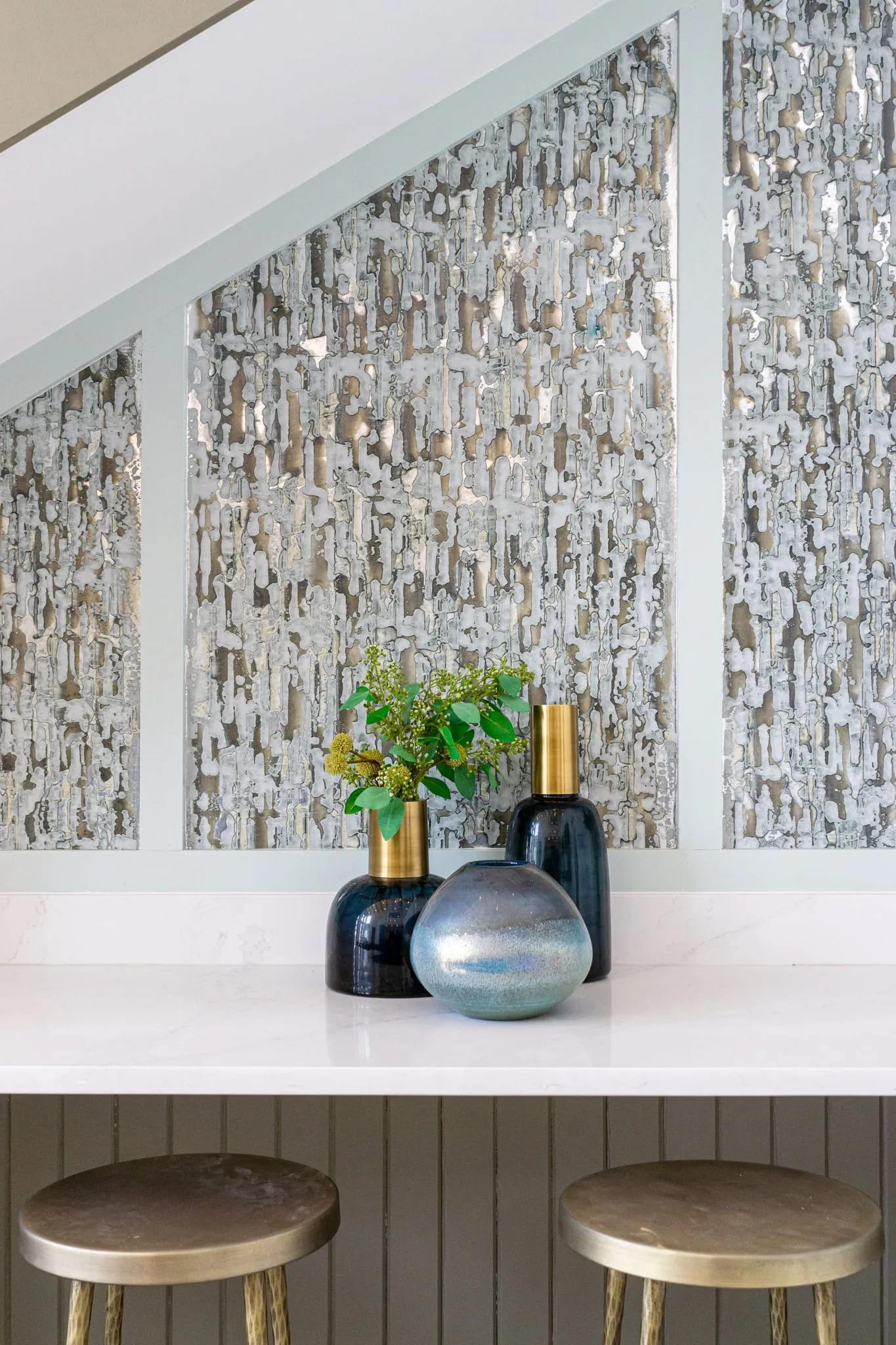 Multifamily bar counter with a textured stone-look wallcovering above the white counter and two brass stools