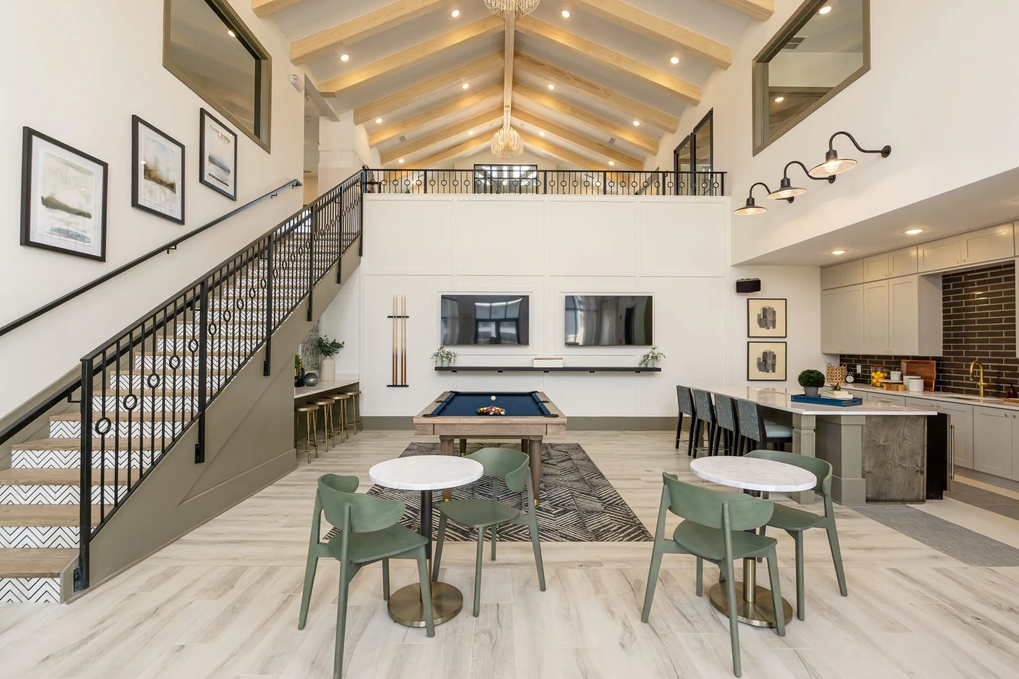 Multifamily amenity double-height clubroom, framed prints up the stair wall, billiards and cafe tables below the vault