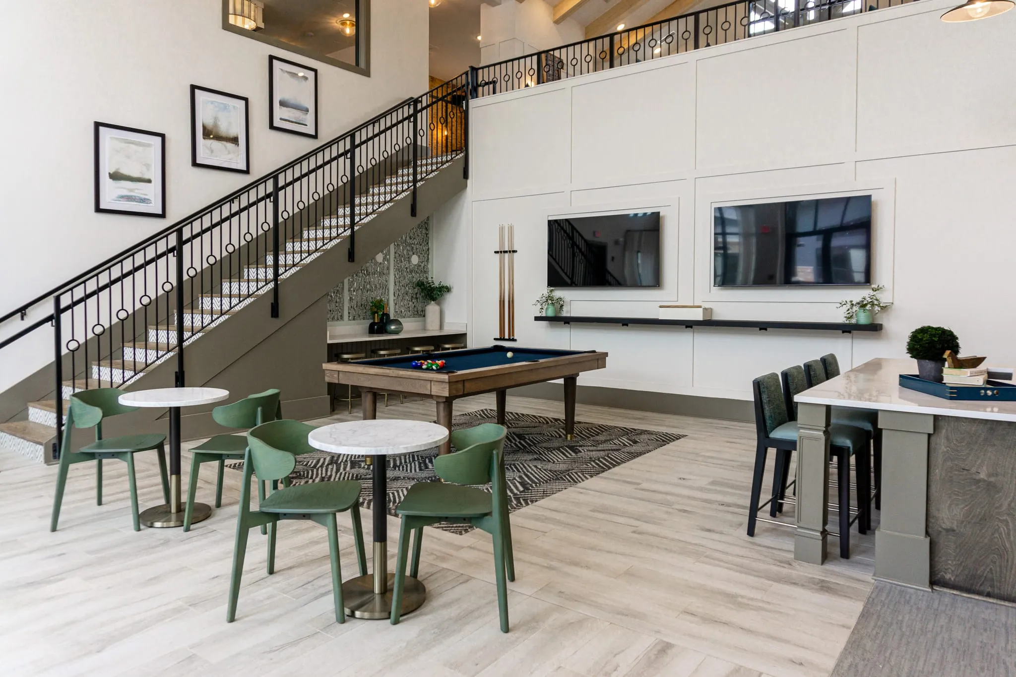 Multifamily amenity clubroom with a billiards table and sage cafe chairs below the iron stair and mezzanine