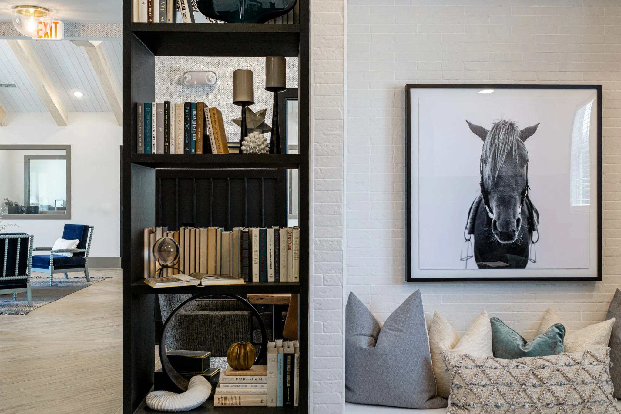 Multifamily amenity library with black shelving beside a framed horse portrait above a cushioned bench seat