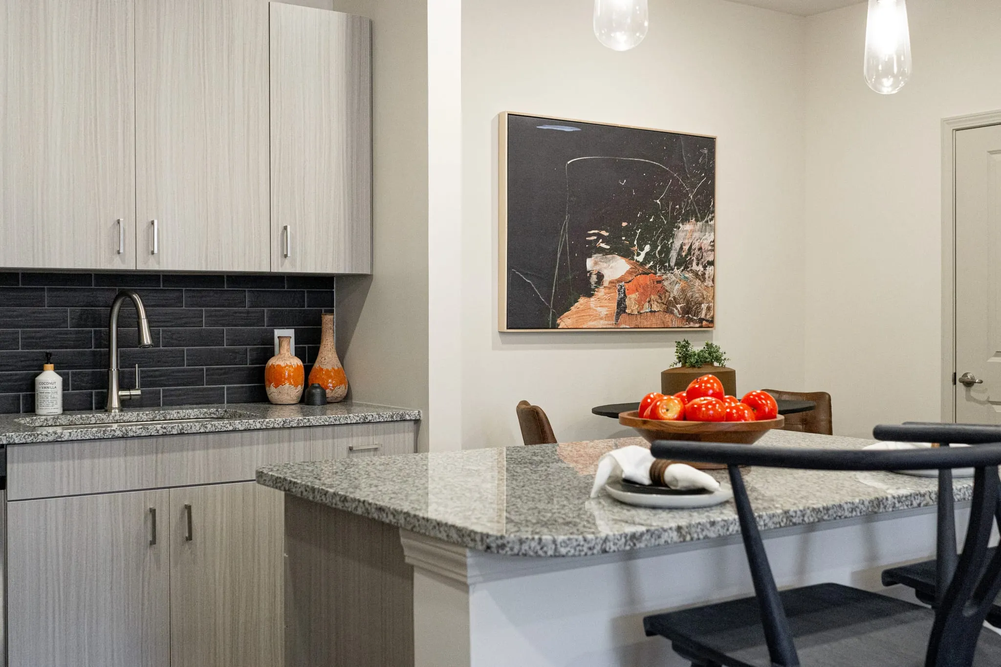 Multifamily model apartment kitchen with a granite island and grey cabinetry, charcoal subway tile backsplash