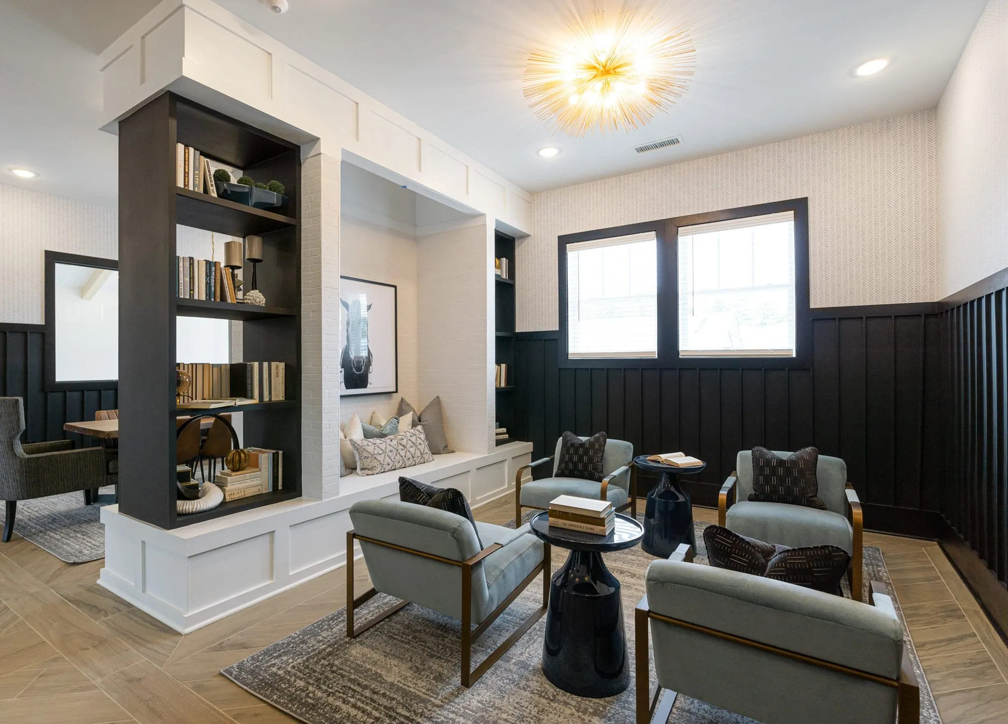 Multifamily amenity study with a built-in bookcase divider and sage chairs against black board and batten panelling