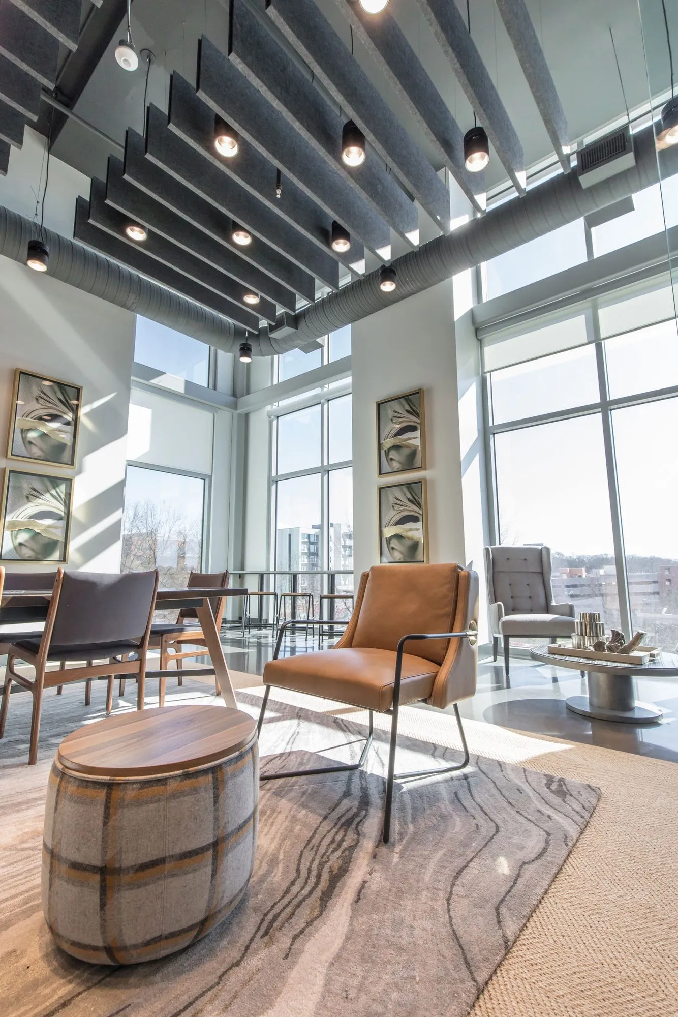 Multifamily amenity double height lounge with a barrel side table, tan leather chair and slatted ceiling with globe pendants