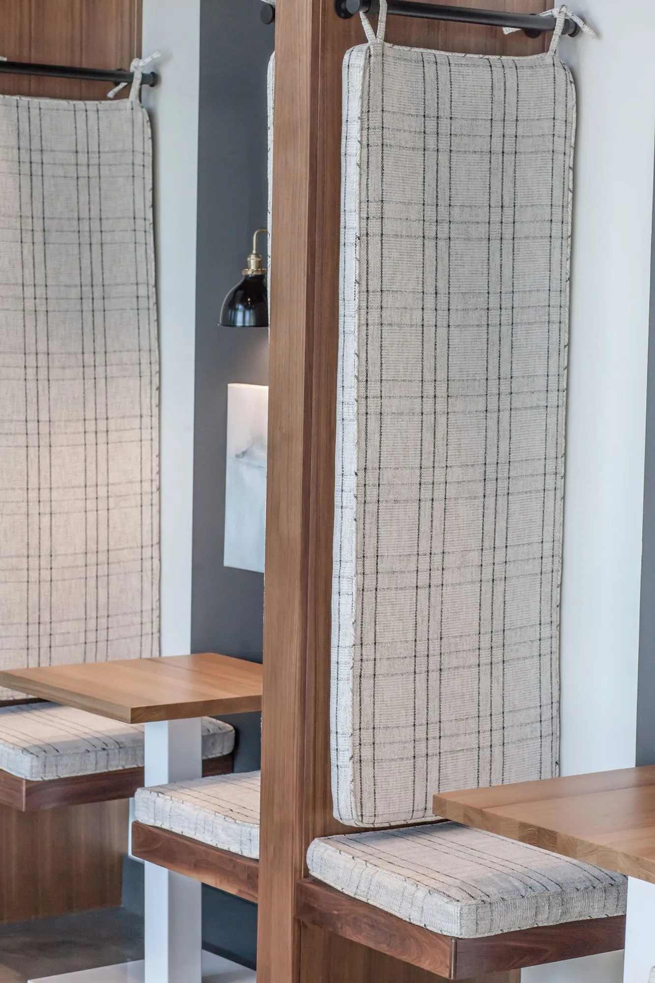 Multifamily amenity work booth detail: plaid upholstered seat and back cushions hung from black rails on wood booths