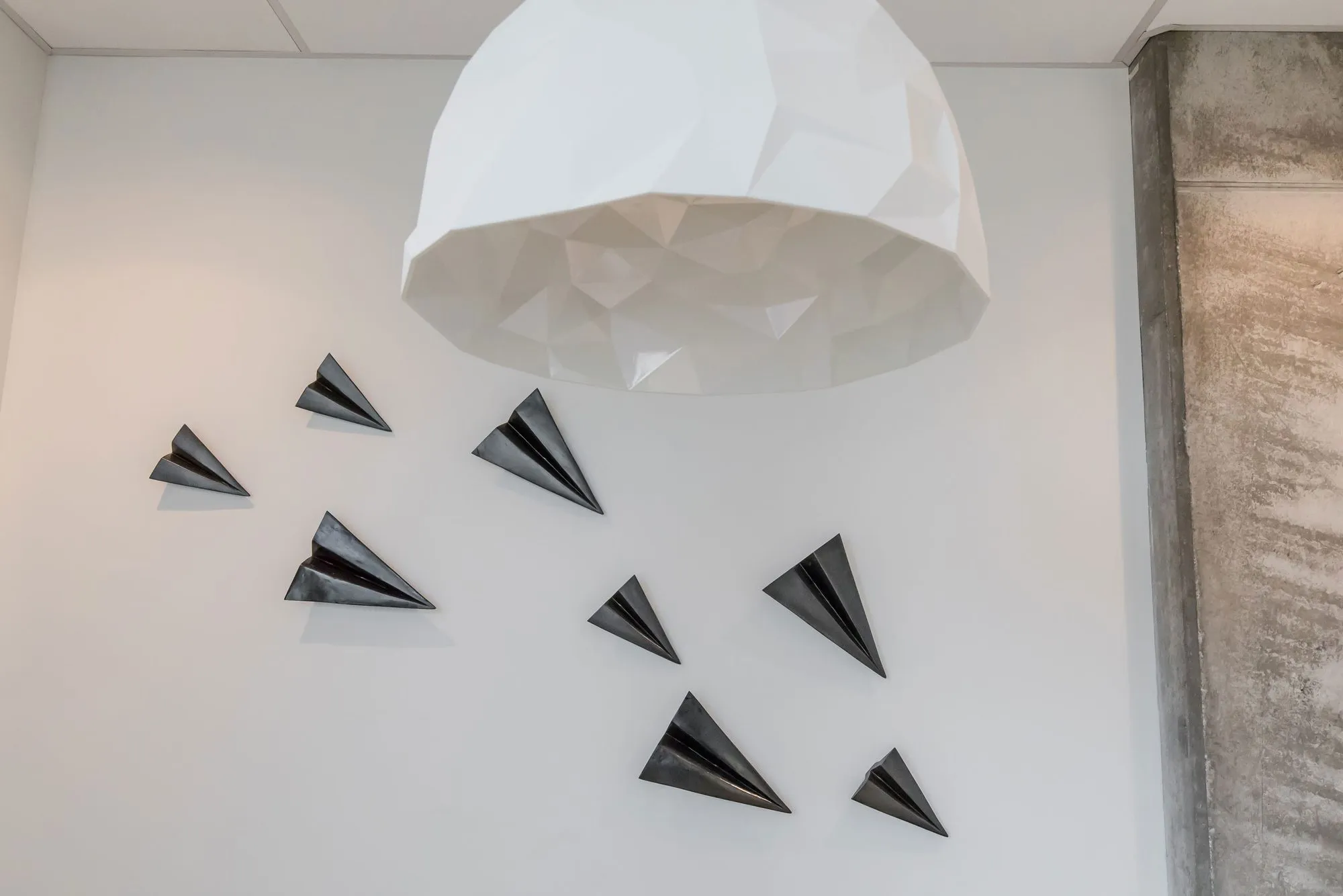 Multifamily interior detail: black folded paper planes mounted on a white wall below a faceted white dome pendant