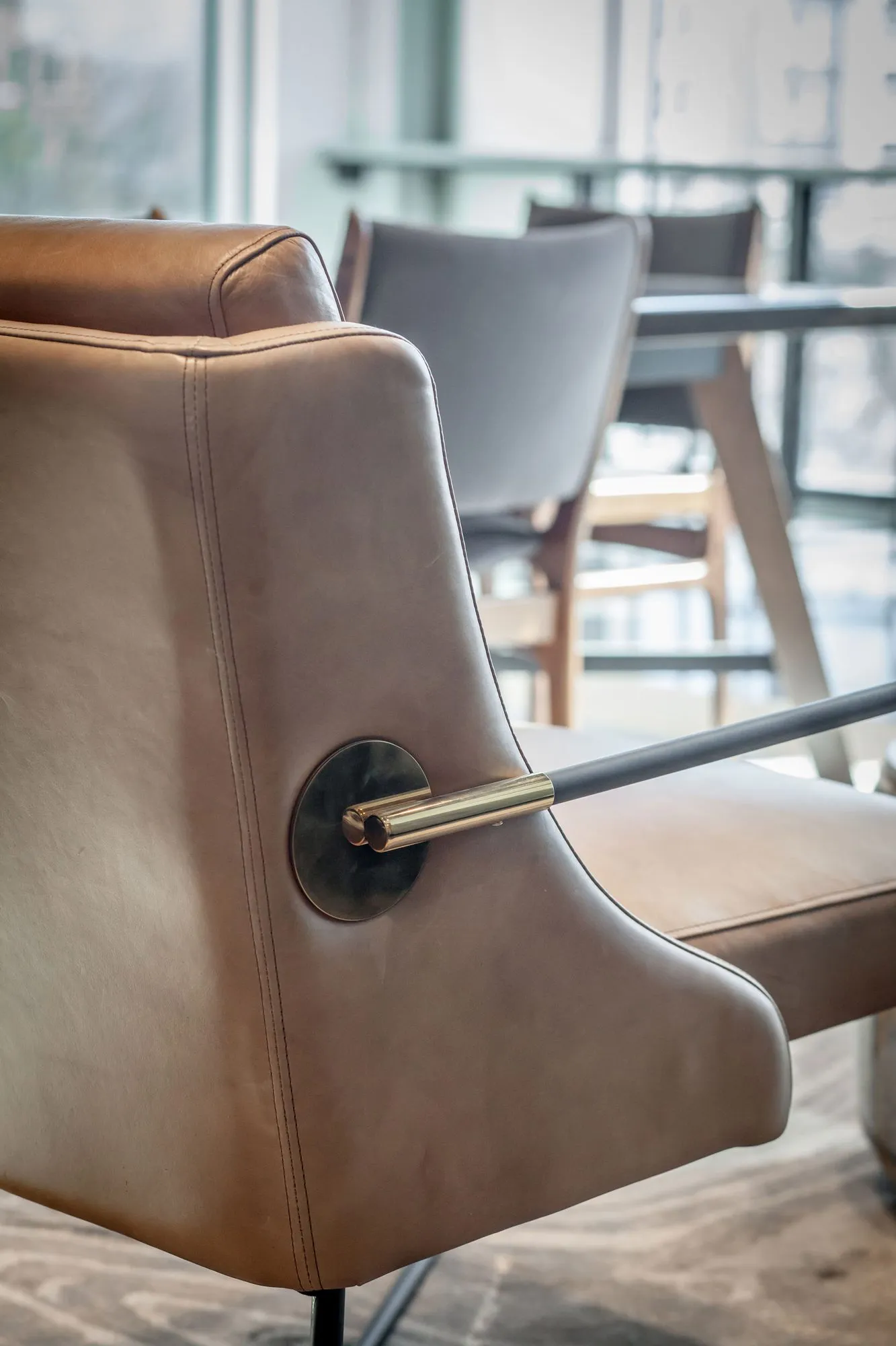 Multifamily interior detail: leather lounge chair with a brass and black arm bar beside a dining table