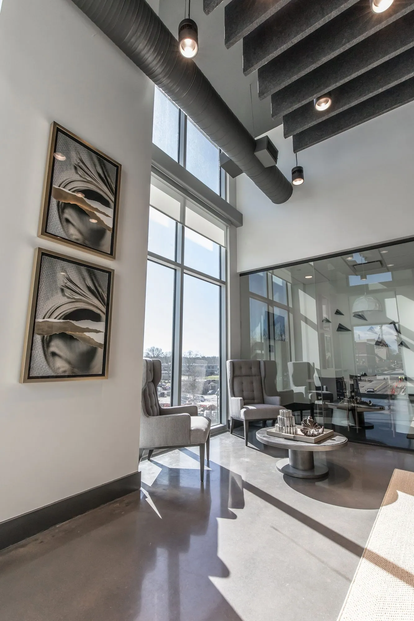 Multifamily seating area with grey wingback chairs and a round table below tall windows and framed face portraits