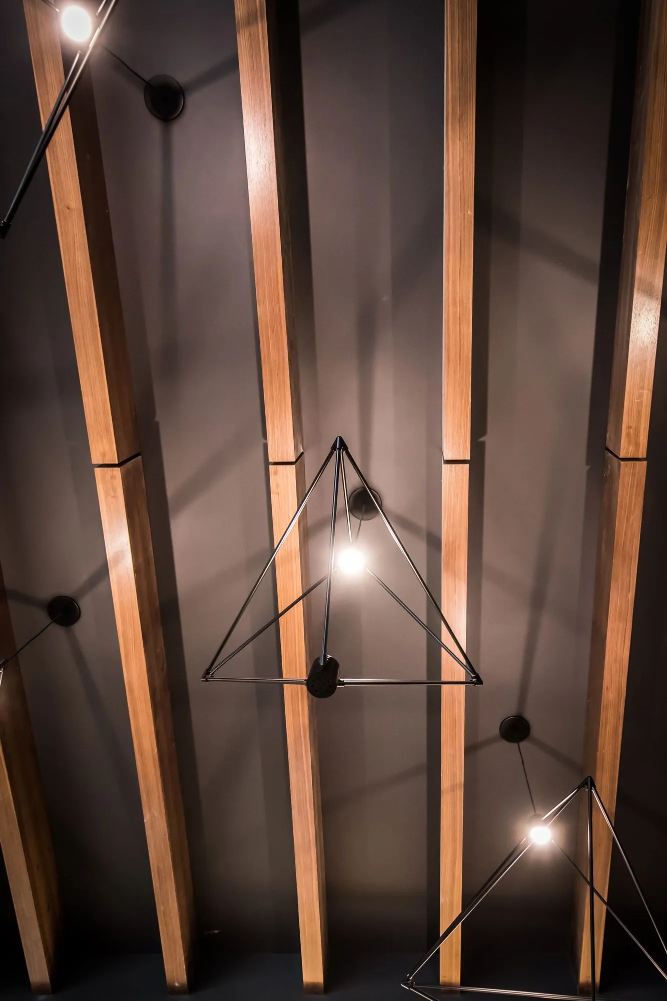 Multifamily interior detail: looking up at timber ceiling beams and black wire pyramid pendants with exposed bulbs