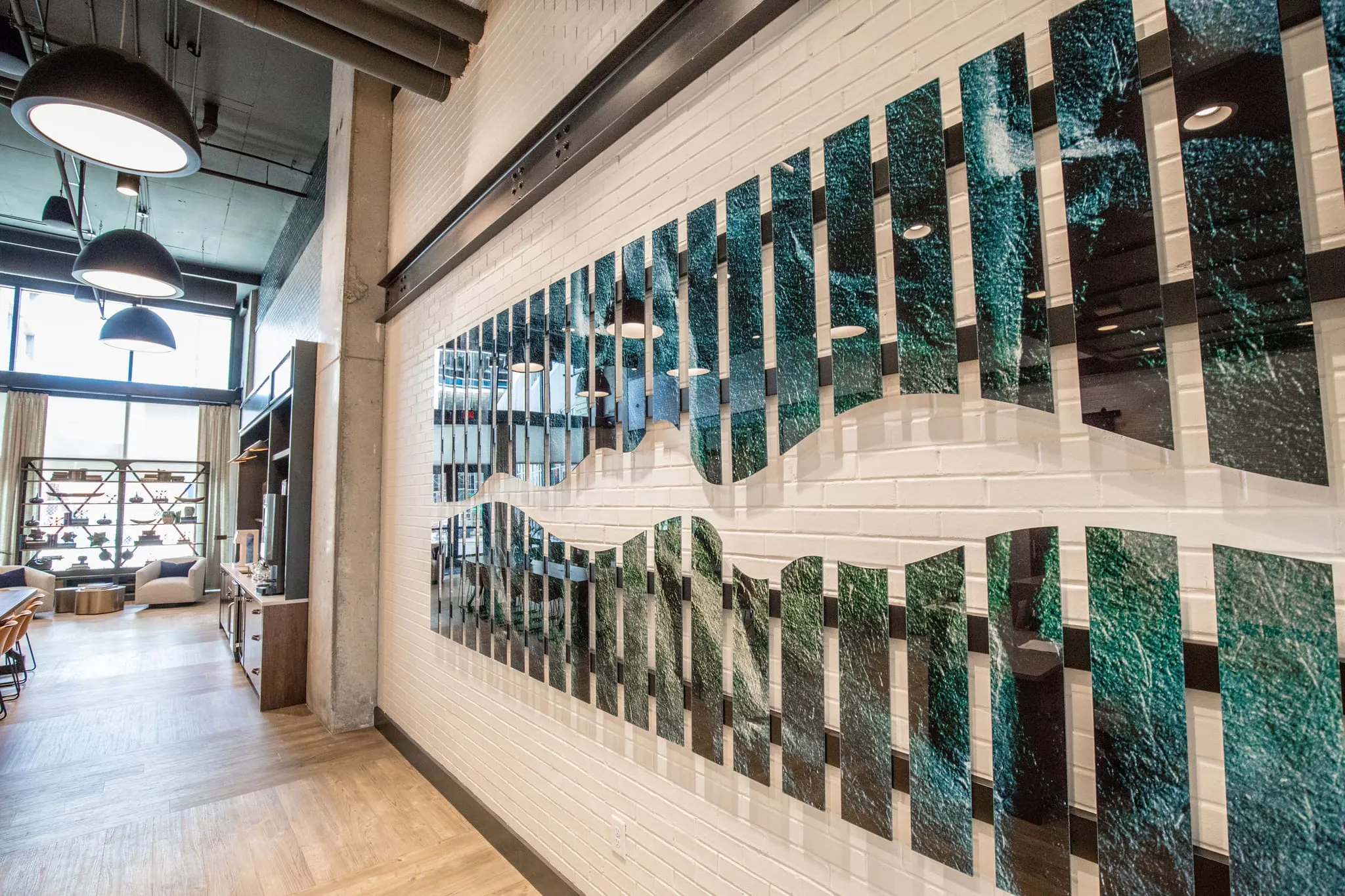 Multifamily amenity lounge with a book art installation, a wall of teal painted book spines under black dome pendants