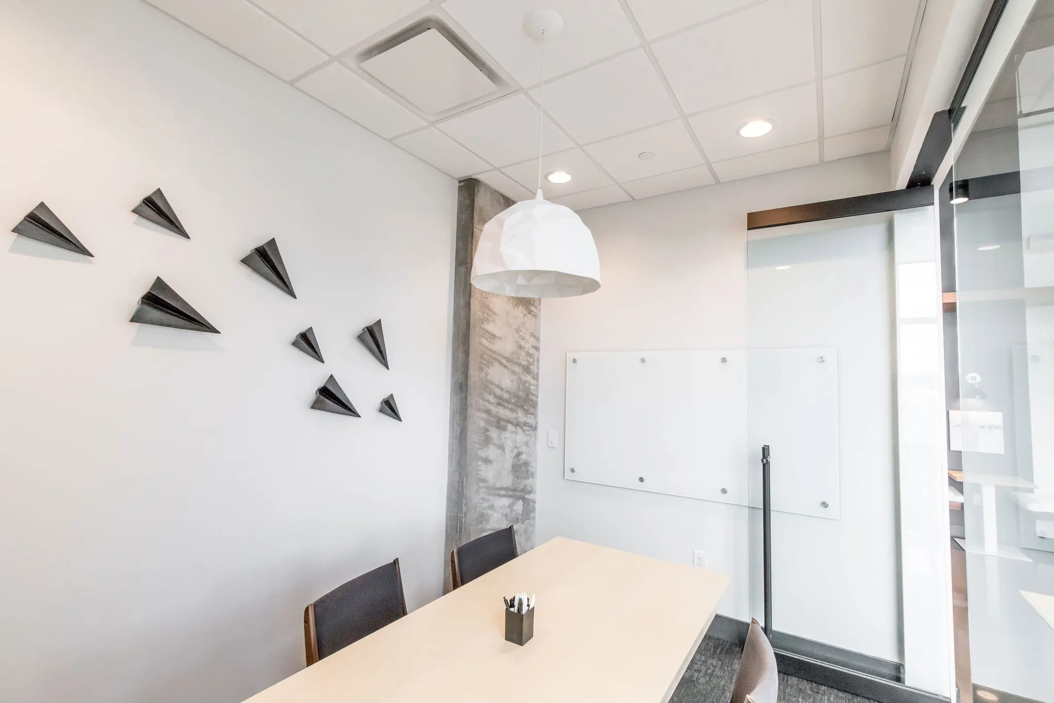 Multifamily amenity conference room with a pale wood table under a white pendant, black paper plane sculptures on the wall