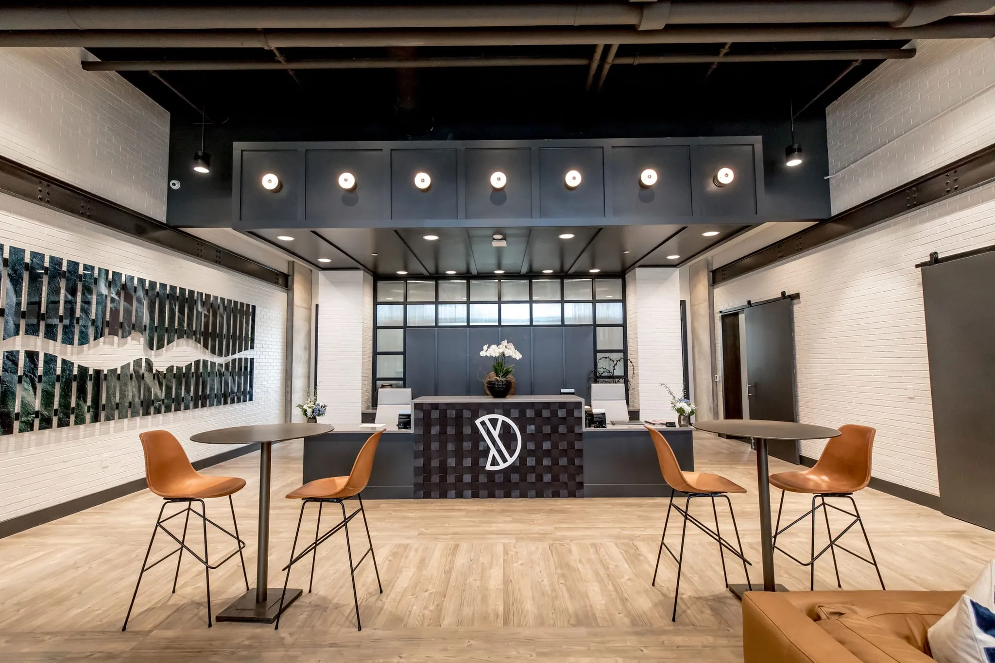 Multifamily amenity lobby with a dark reception desk under a soffit of round lights, tan stools at high tops, glass art