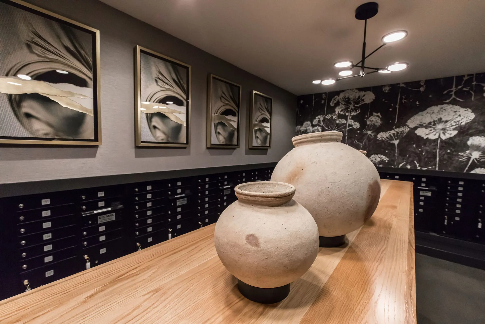 Multifamily amenity mail room with black mailboxes below framed black and white photographs, two clay vessels on the counter
