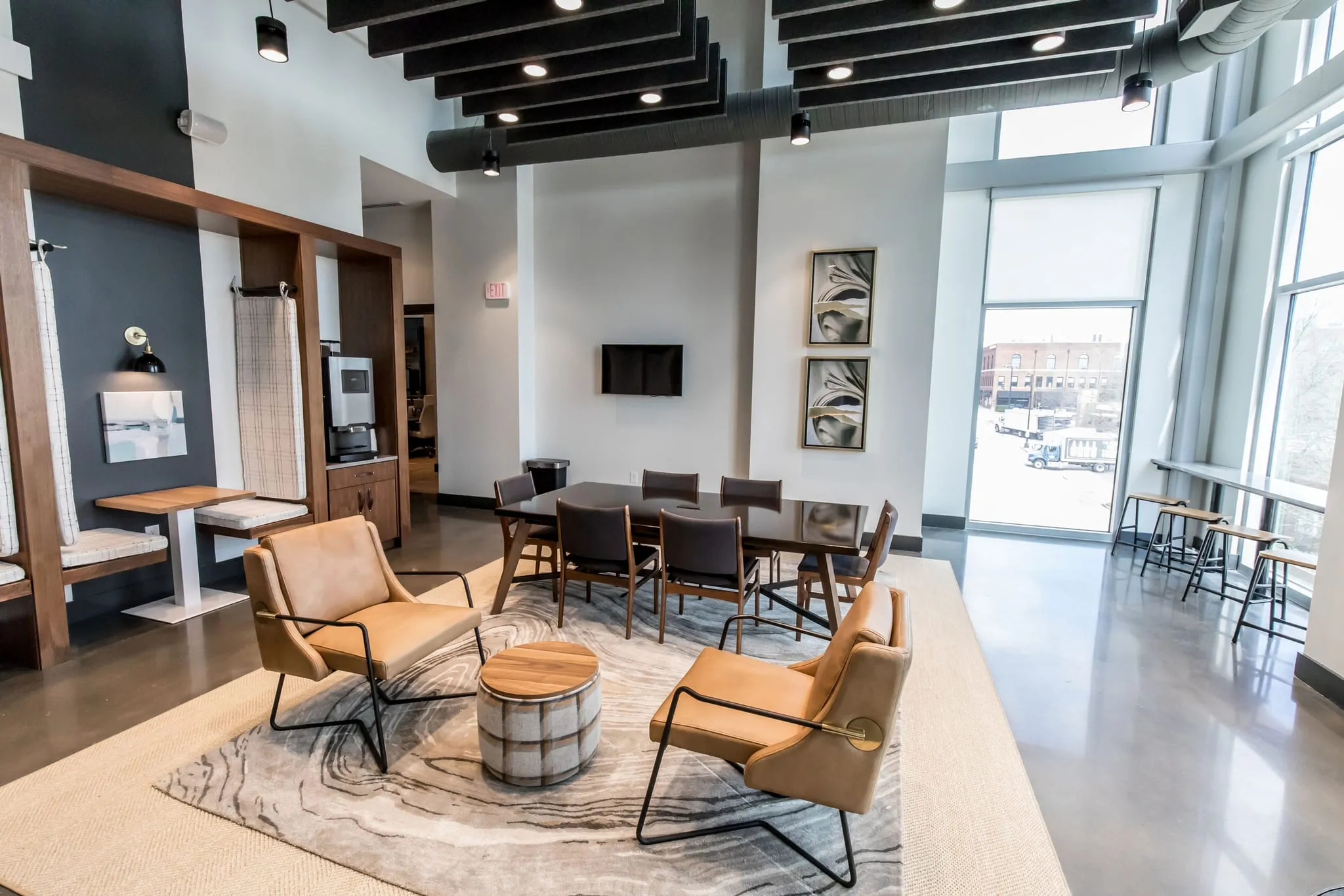Multifamily amenity resident lounge with leather sling chairs and a drum ottoman under black ceiling baffles by tall glazing