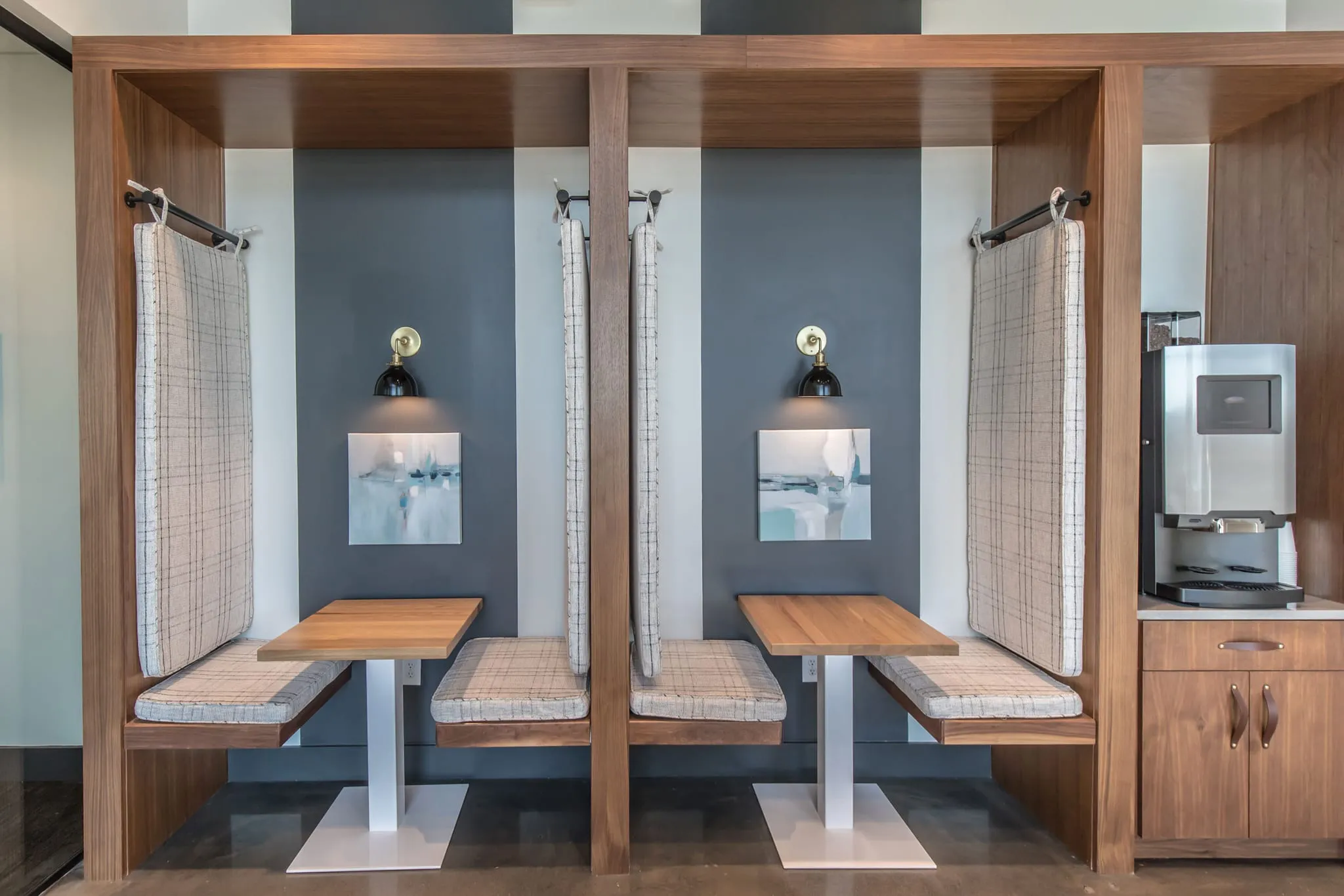 Multifamily amenity work booths: two curtained wood booths with sconces beside the coffee machine