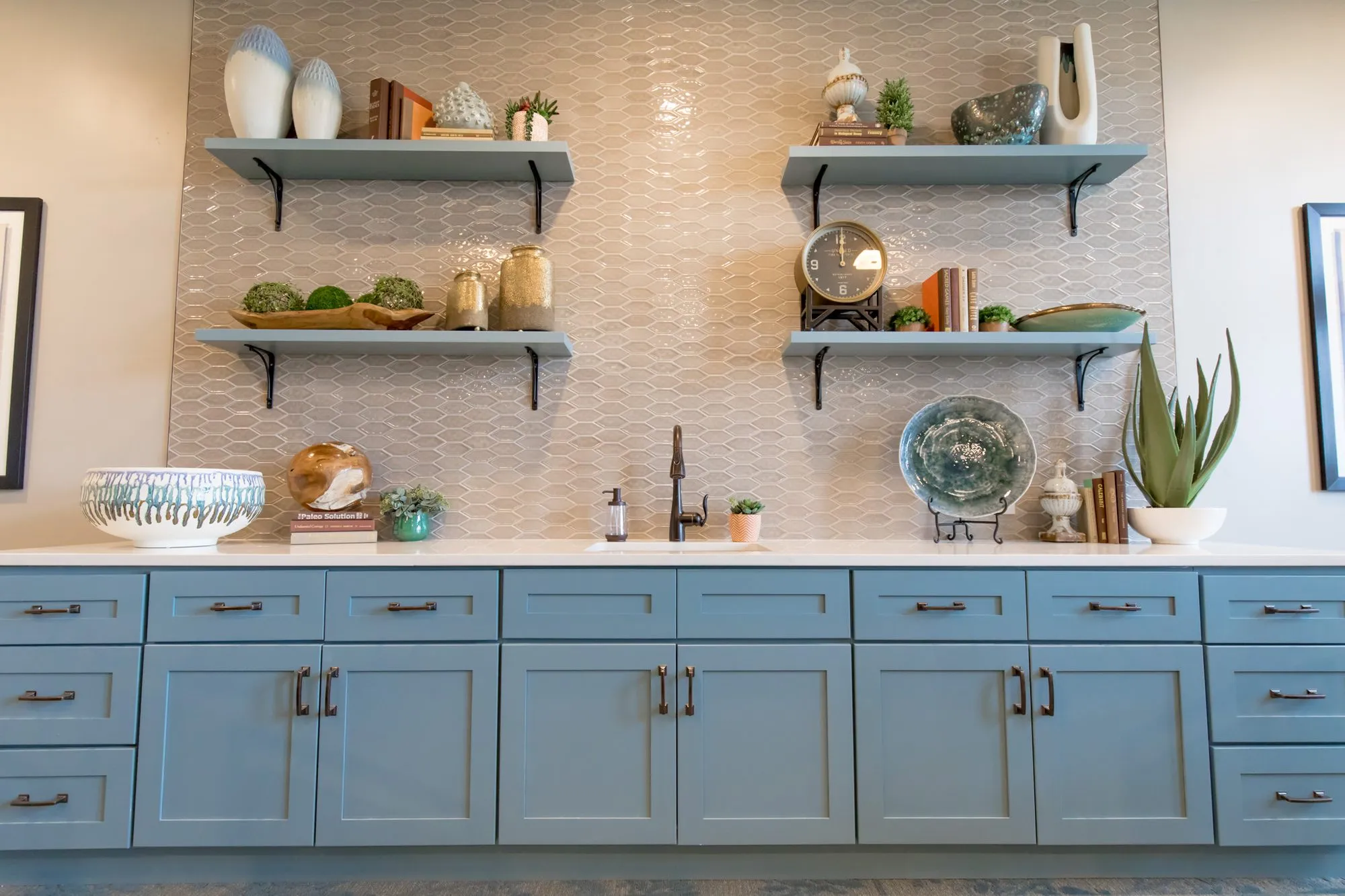 Senior living interior detail: blue shaker cabinetry, white counter and open shelving with pottery against iridescent tile