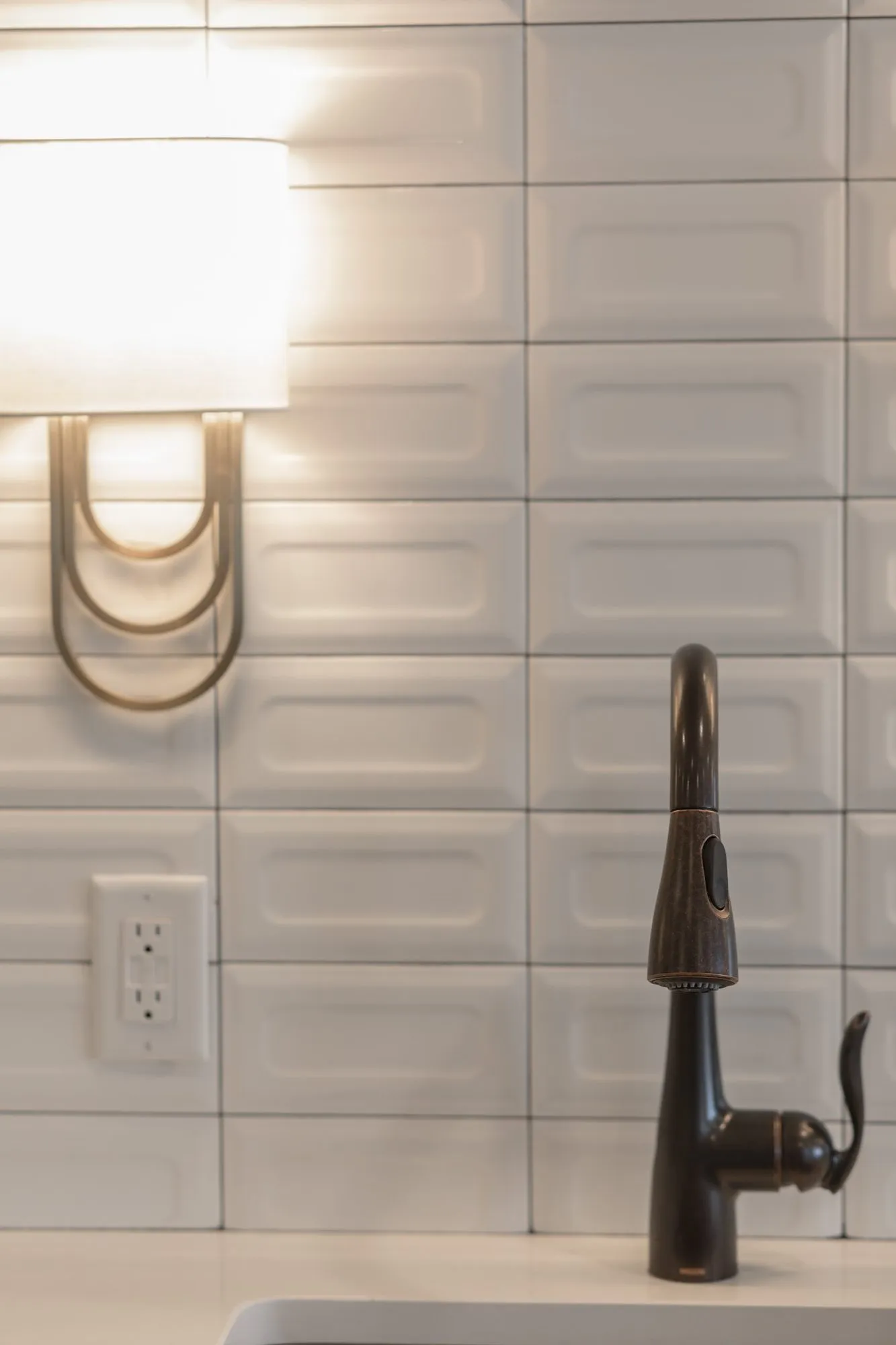 Senior living interior detail: brass loop sconce and dark bronze faucet against white bevelled subway tile