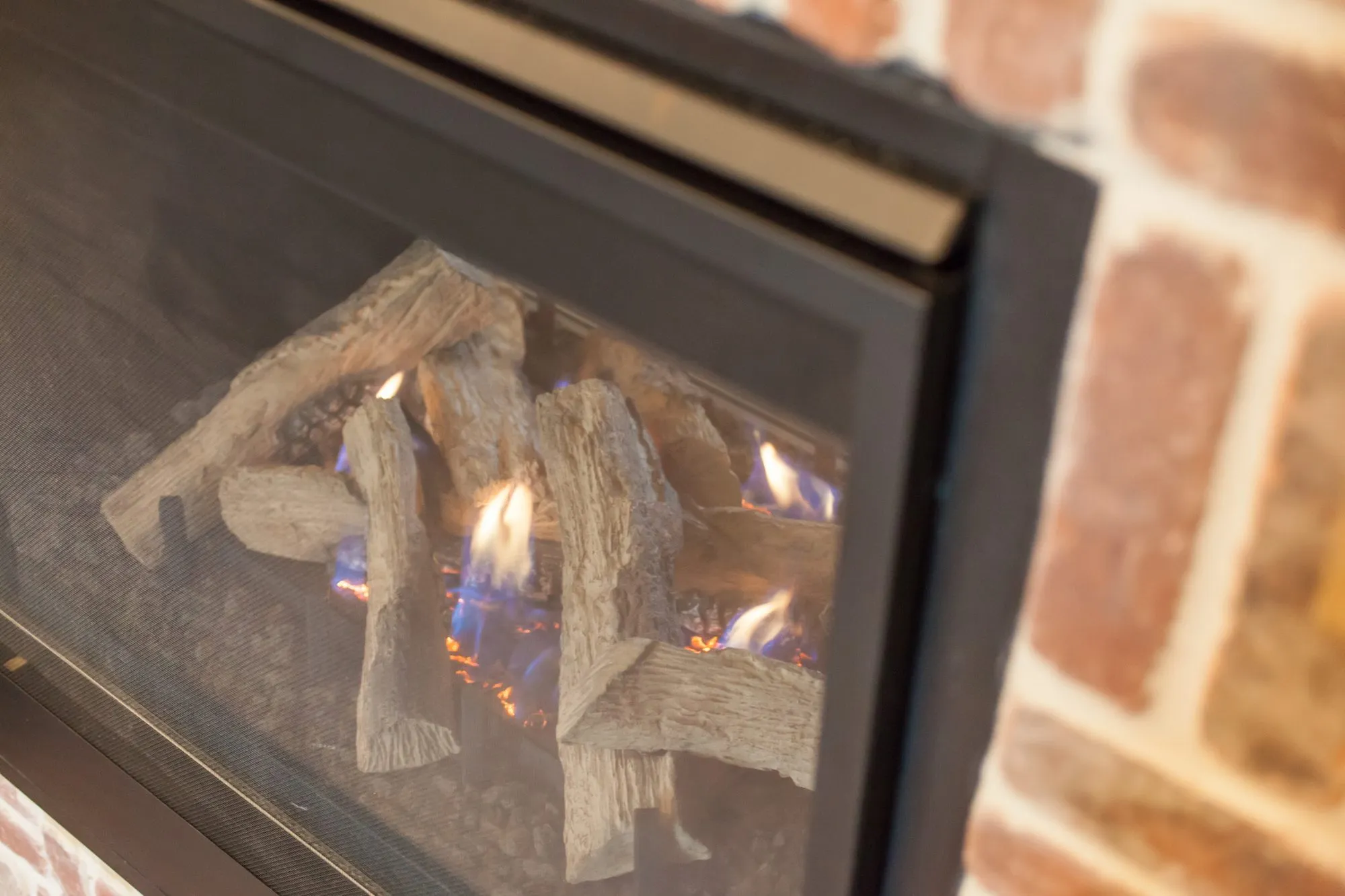 Senior living interior detail: gas fireplace with ceramic logs in a black surround set into brick