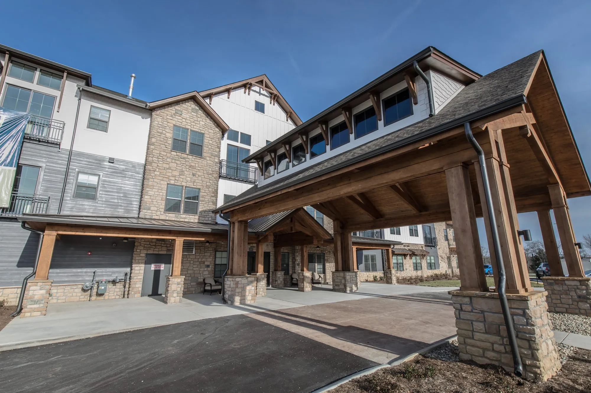 Senior living community exterior: low angle view of the stone and timber porte cochere, residential wings beside it
