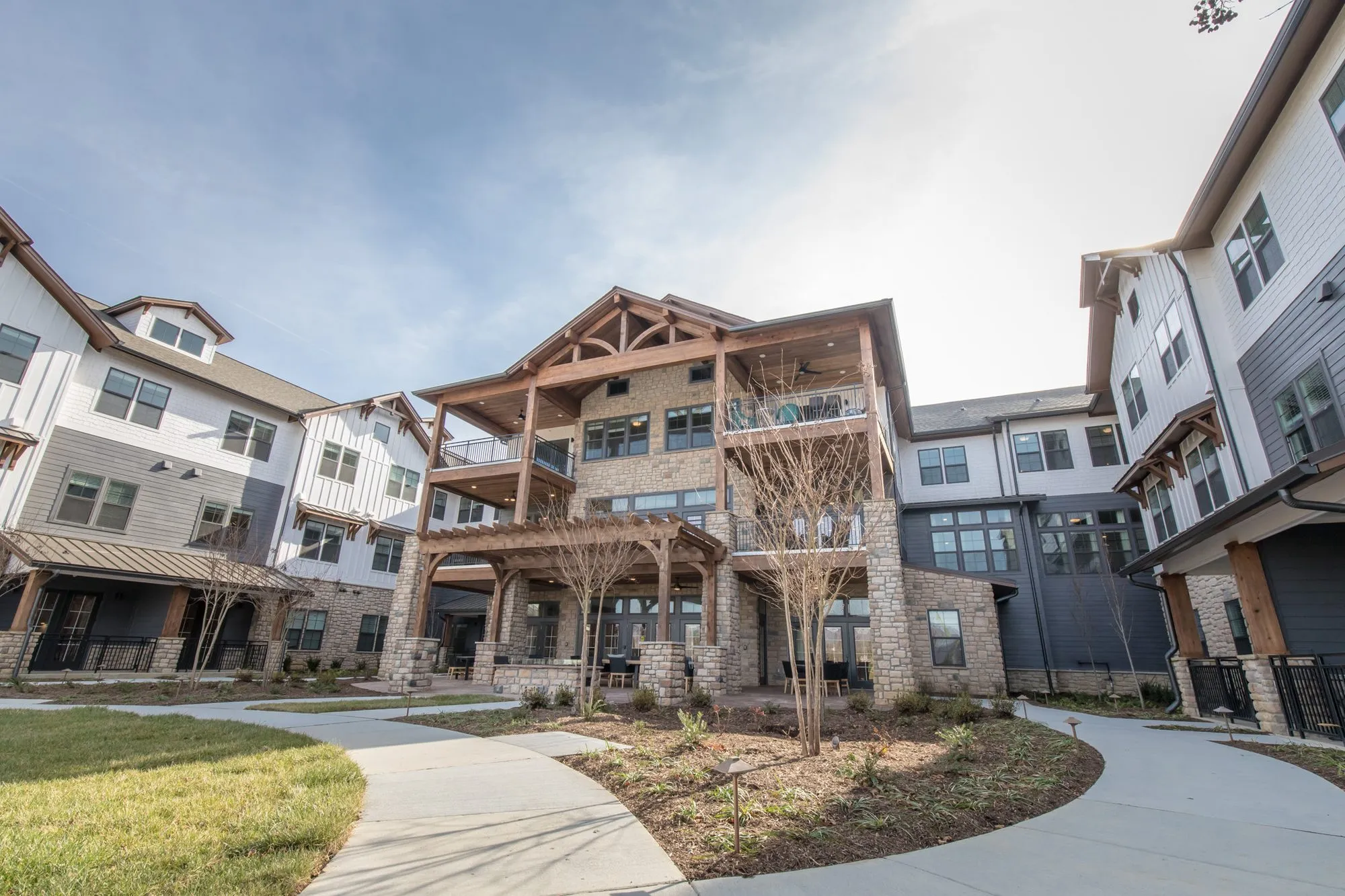 Senior living courtyard with curving paths leading to a stone and timber porch tower between clapboard residential wings