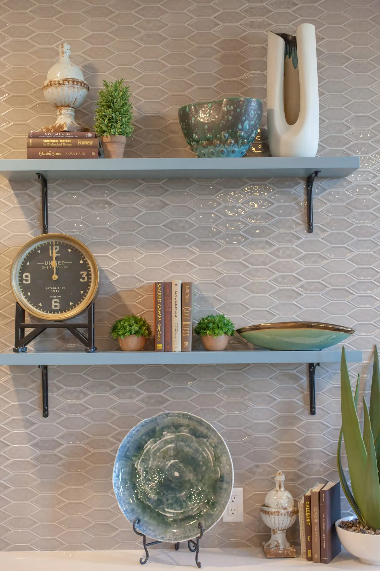 Senior living interior detail: grey shelves with a clock, books, plants and pottery against elongated hexagon tile