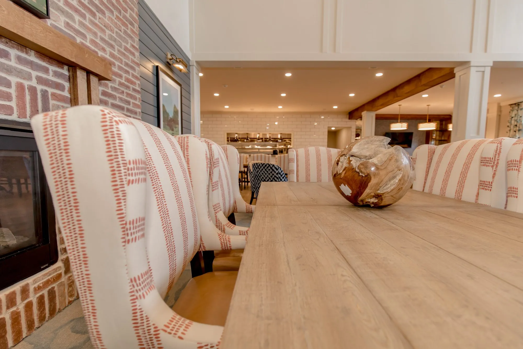 Senior living dining table lined with orange striped wingback chairs beside the brick fireplace